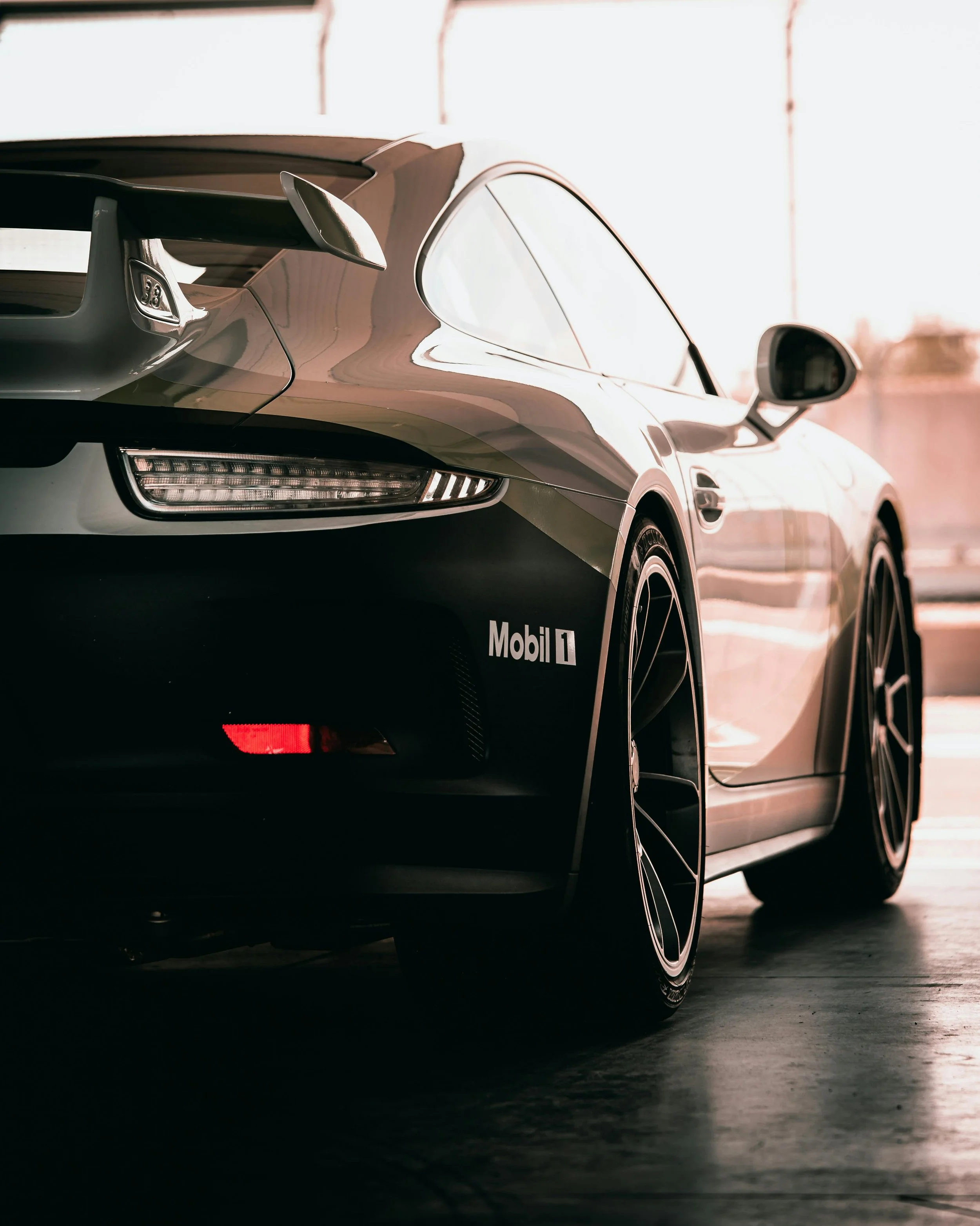 Close-up of a race car's rear end showing a spoiler, rear light, side mirror, and part of the body, with branding including Mobil 1.