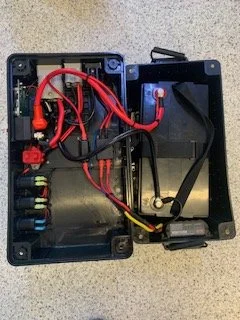 Open plastic electronic enclosure with red and black wires connected to internal components on a gray surface.