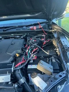 Open car hood showing engine components and wiring.