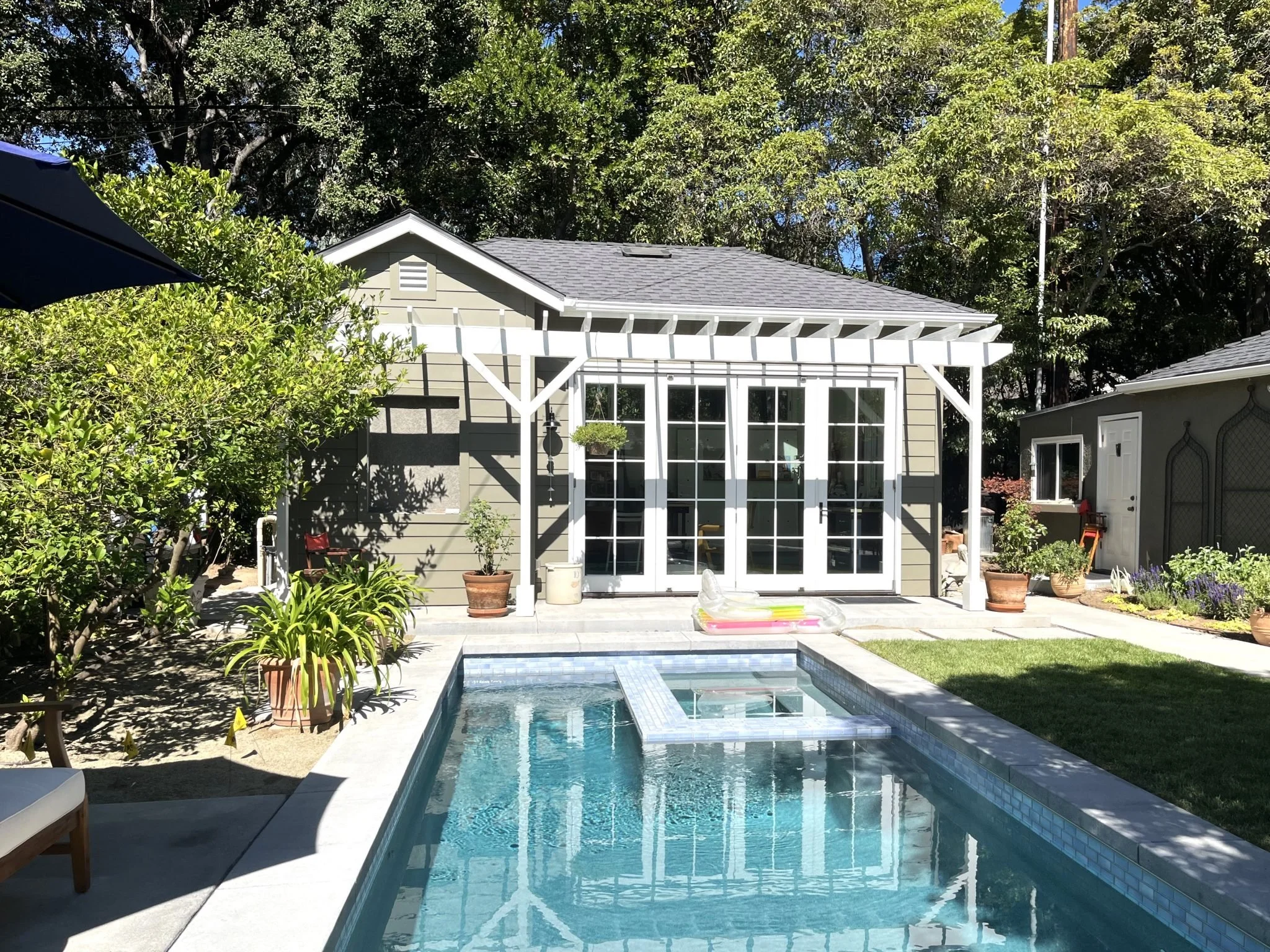 Small gray garden studio with black French doors and a white pergola