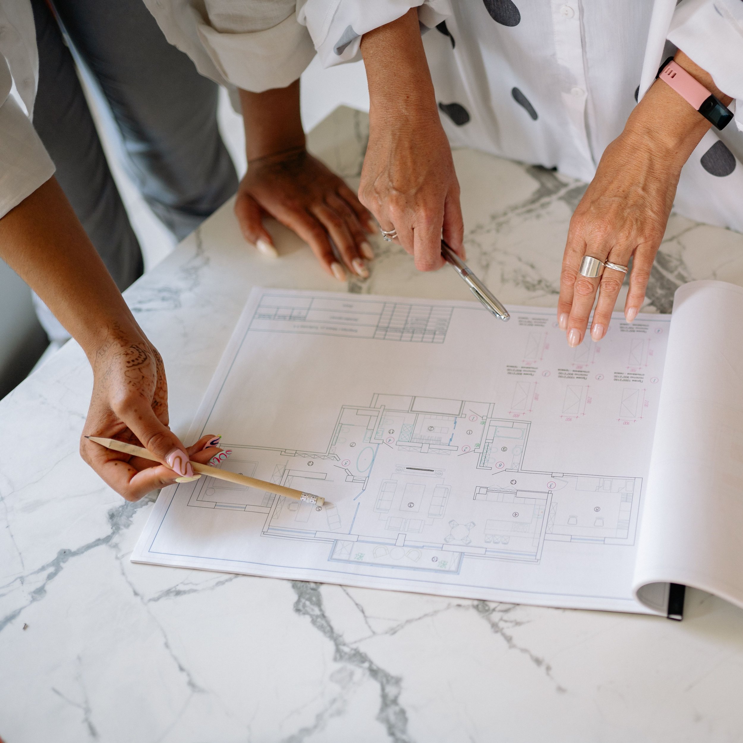 Several people pointing at an architectural floor plan during a design meeting