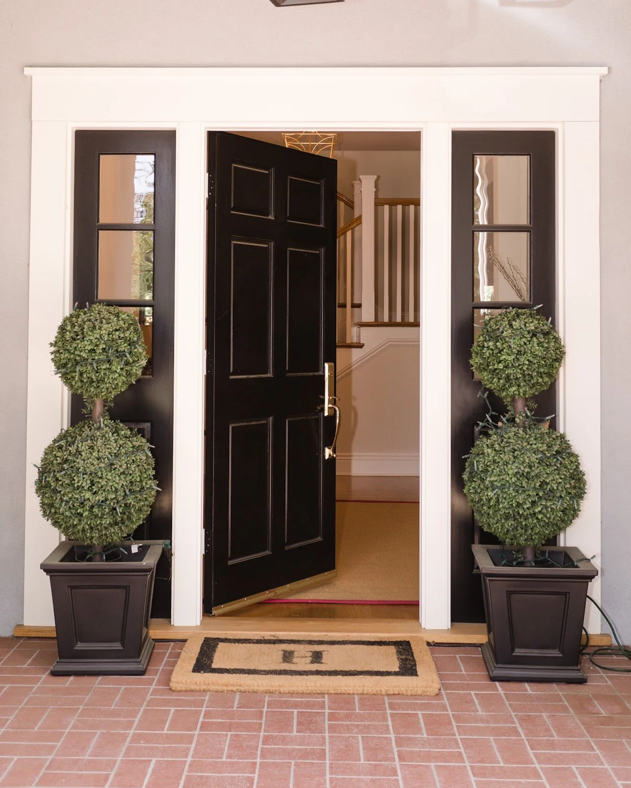 Black front door with sidelights, brick steps and matching topiary planters