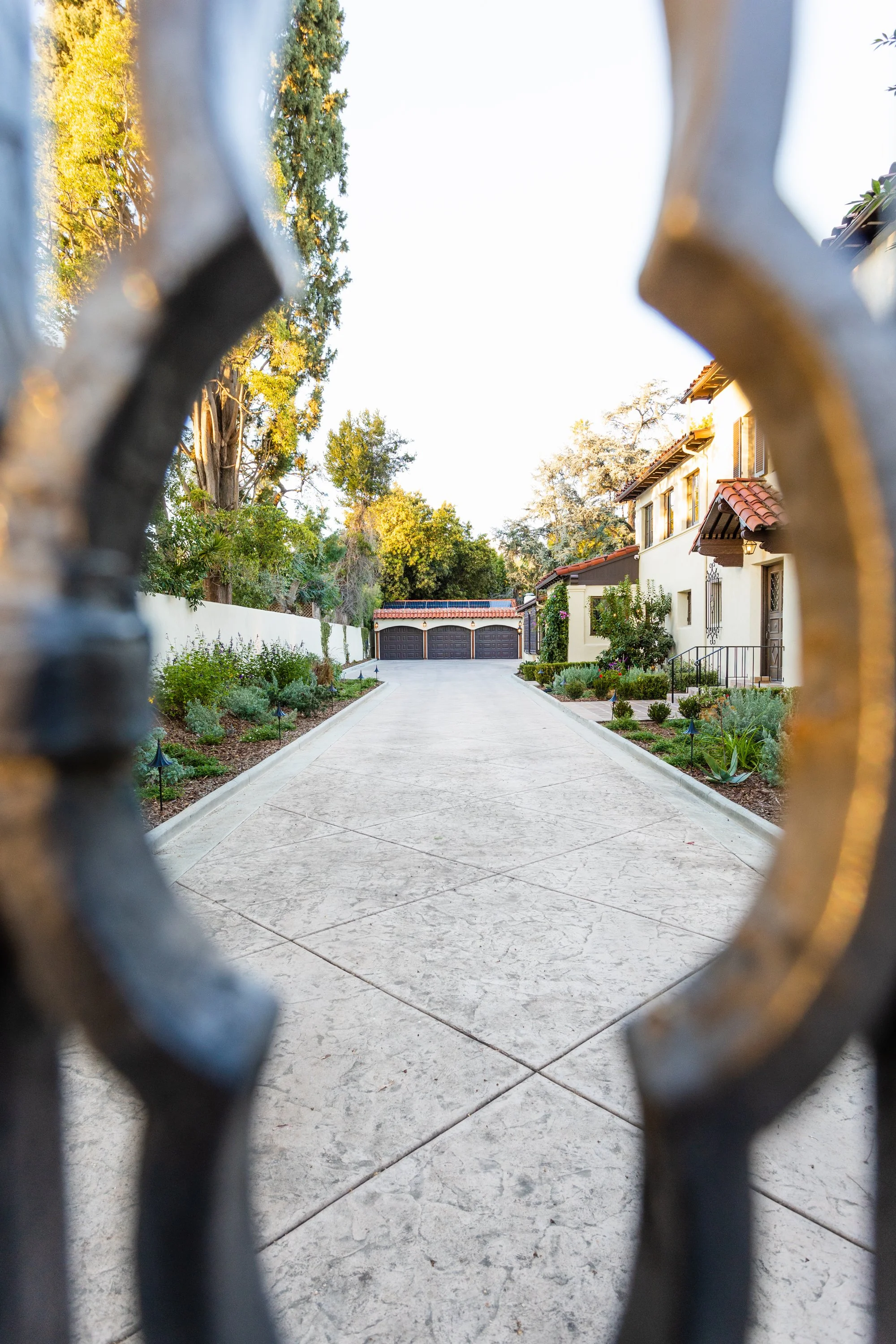 Garage and landscaped driveway viewed through an iron gate