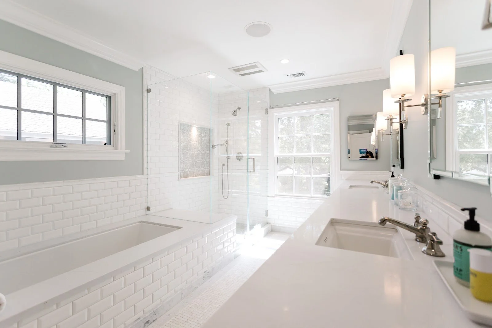 White bathroom with a tiled tub, glass shower enclosure and large window