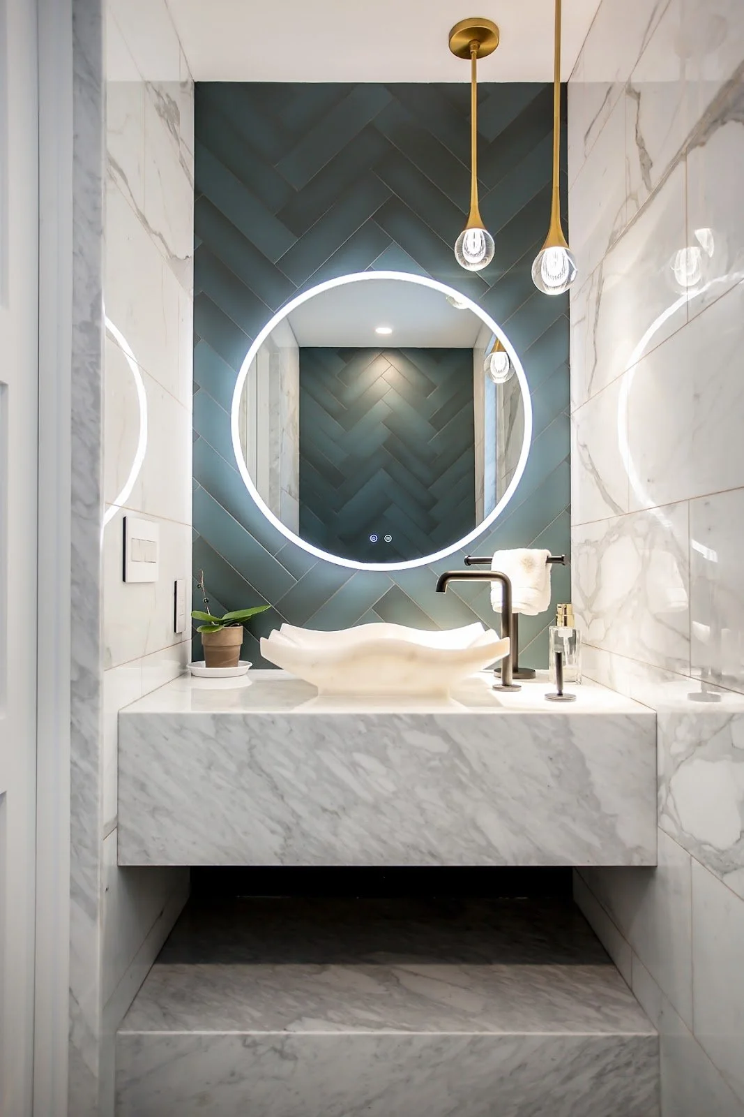 Marble powder room vanity with a round illuminated mirror and herringbone tile