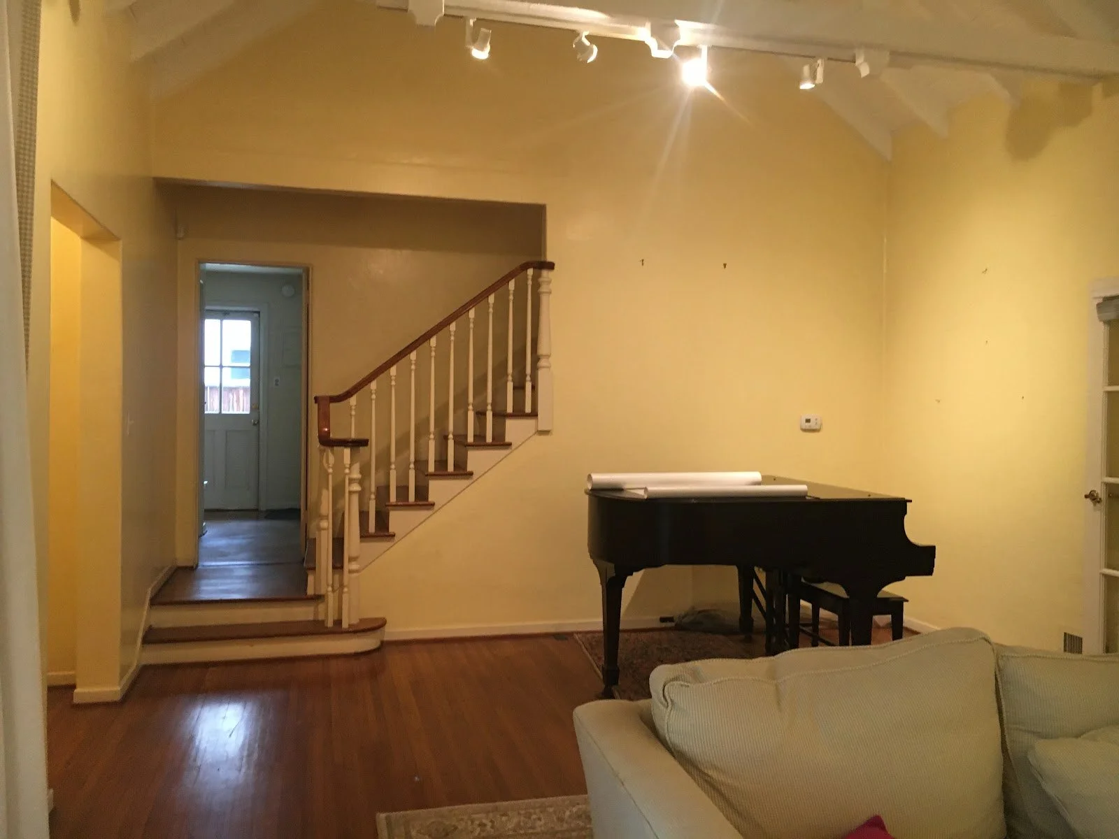 Living room with a grand piano and staircase before renovation