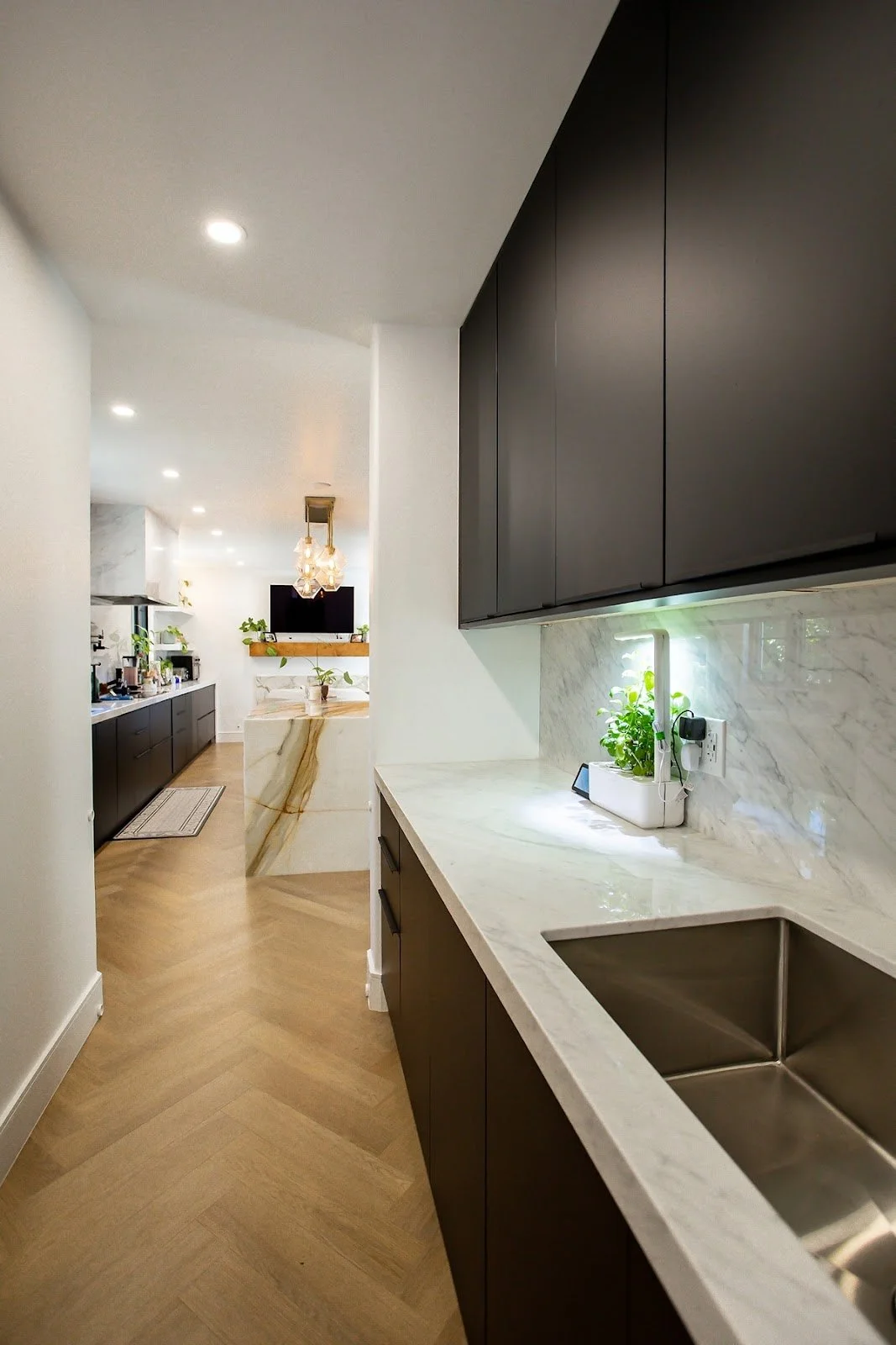 Galley kitchen with dark cabinets, marble counters and herringbone wood floors