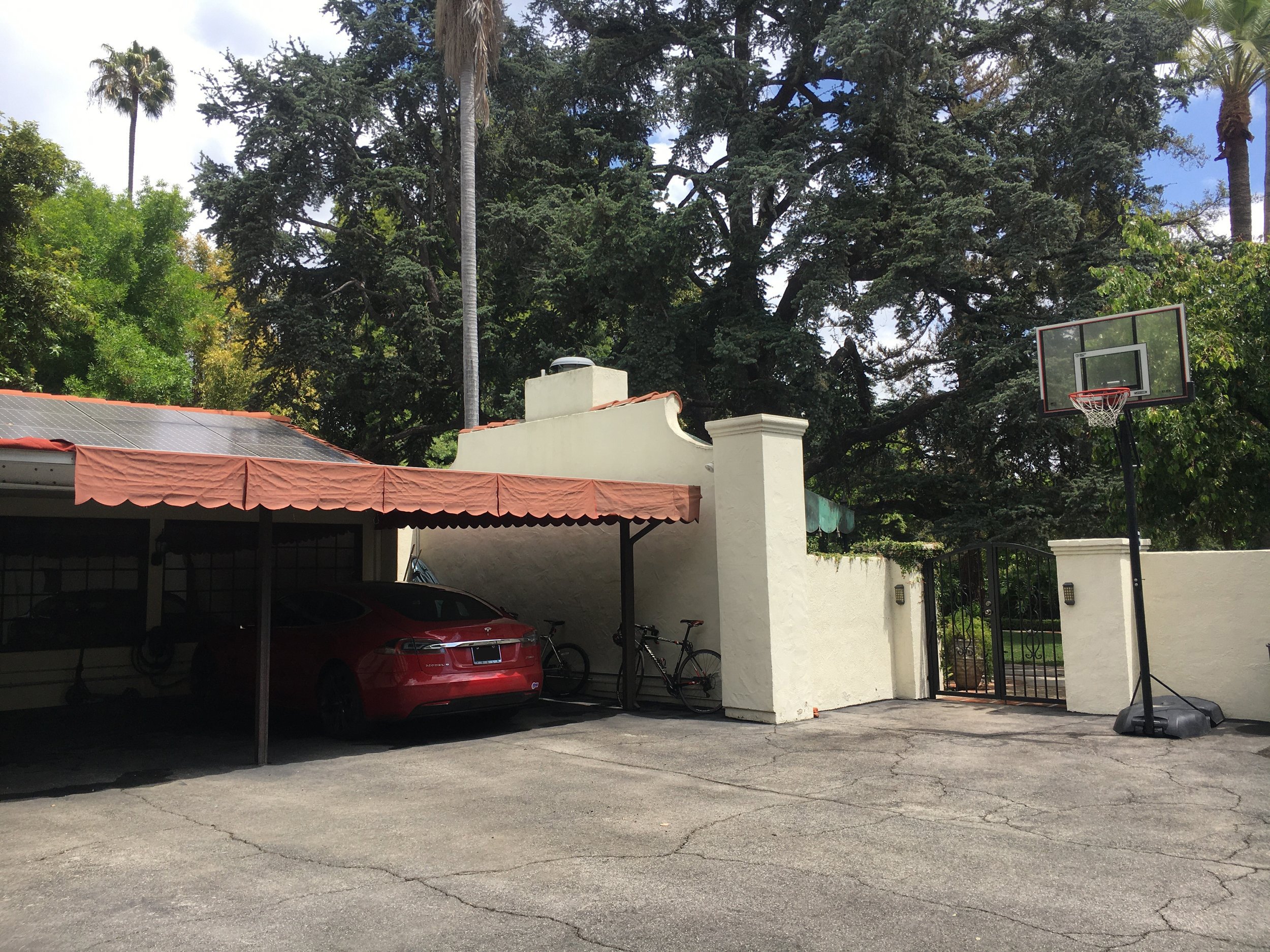 Carport and gated driveway with a basketball hoop before renovation
