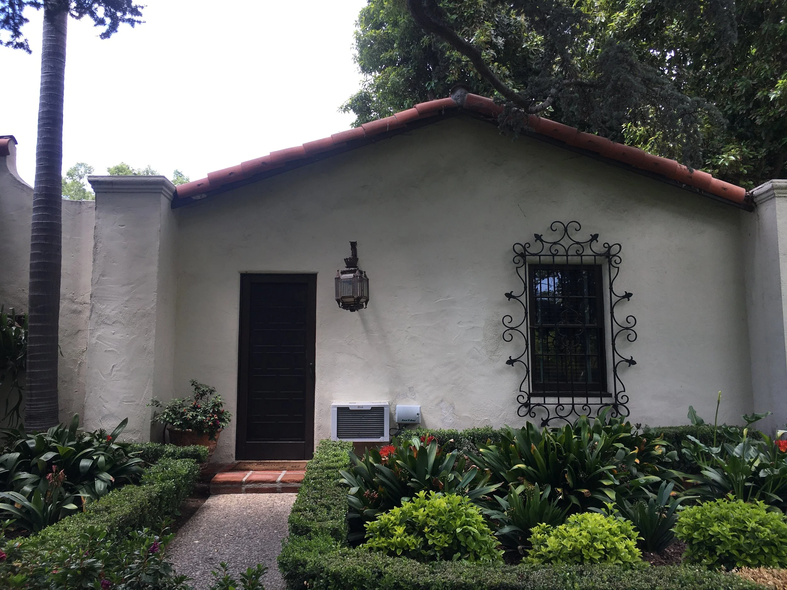 Small stucco side facade and formal garden before renovation