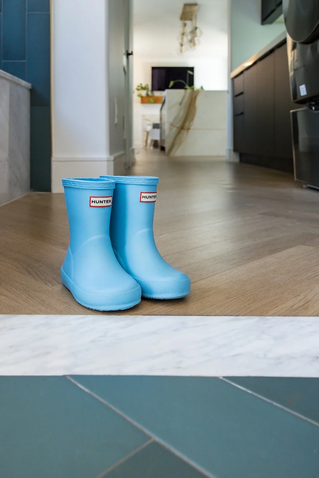 Blue rain boots on herringbone flooring with the remodeled kitchen beyond