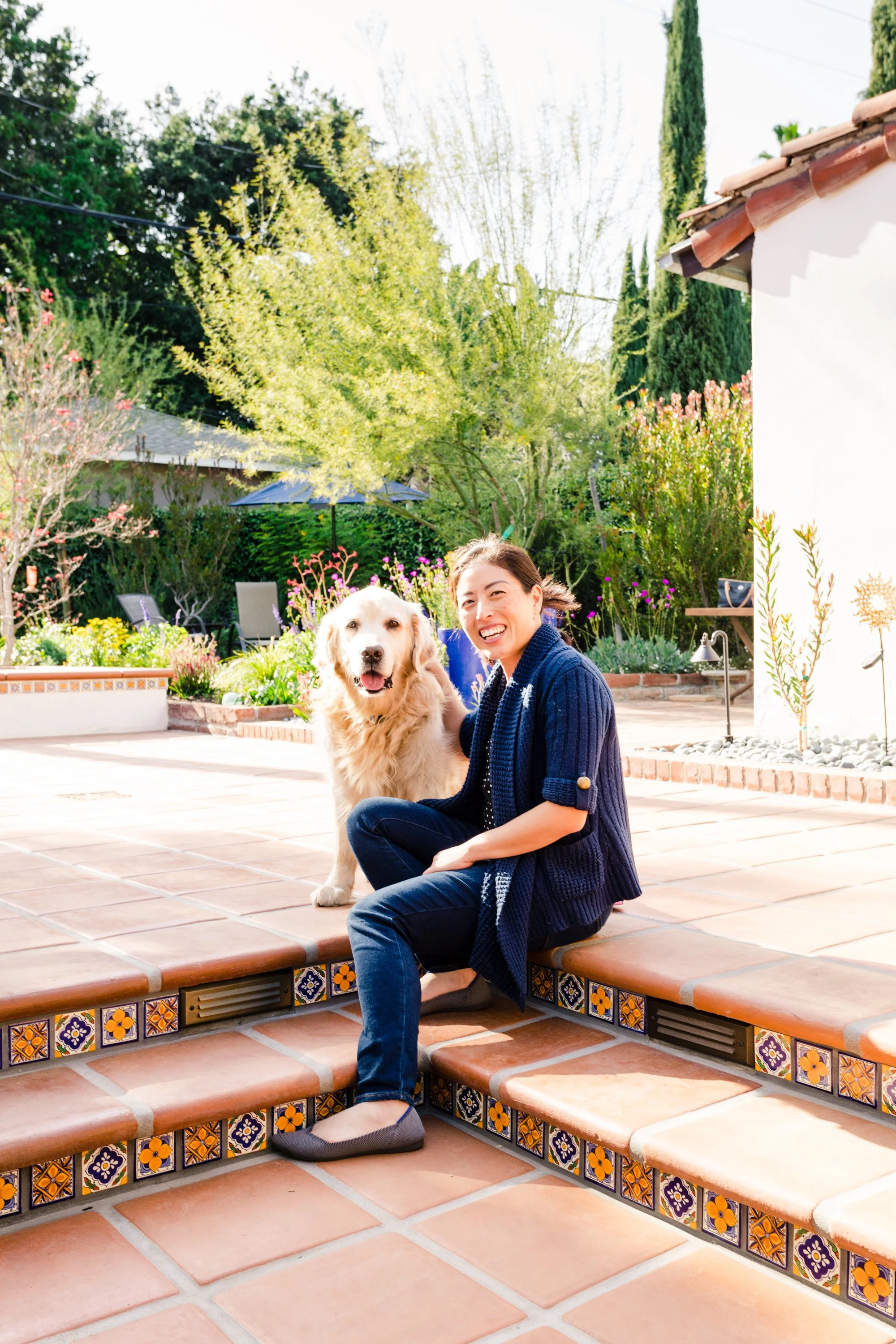 Architect Christina Fu seated beside a golden retriever on a tiled garden patio
