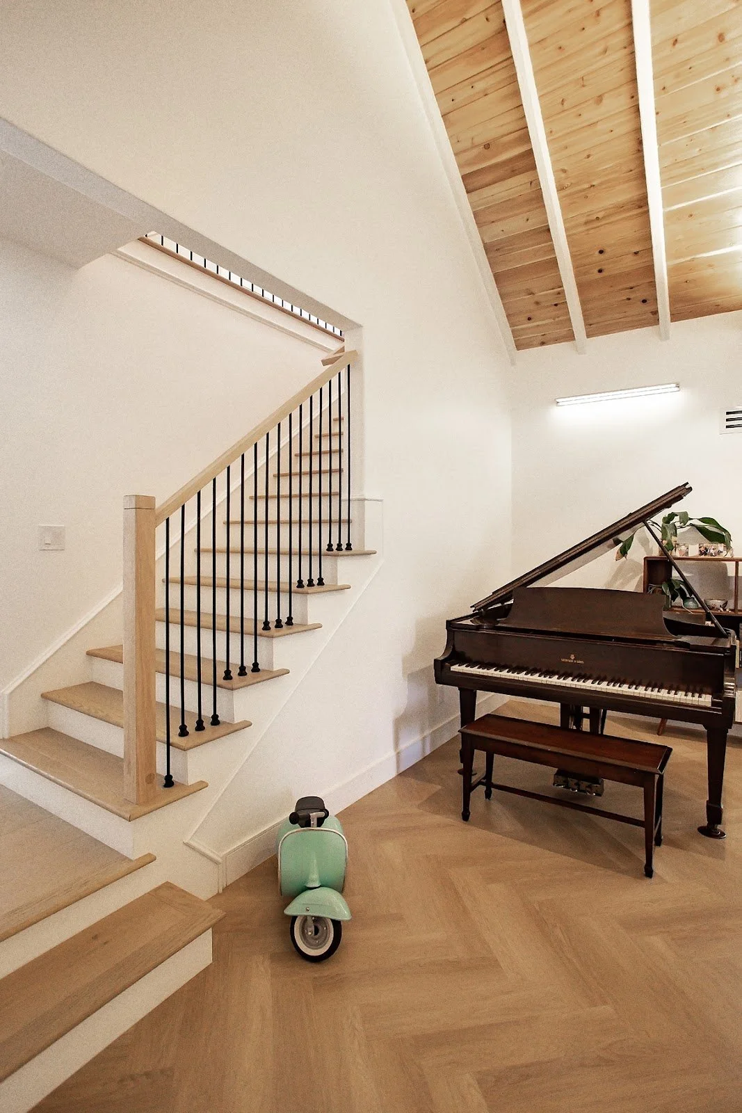 Open staircase beside a grand piano and mint-green ride-on toy