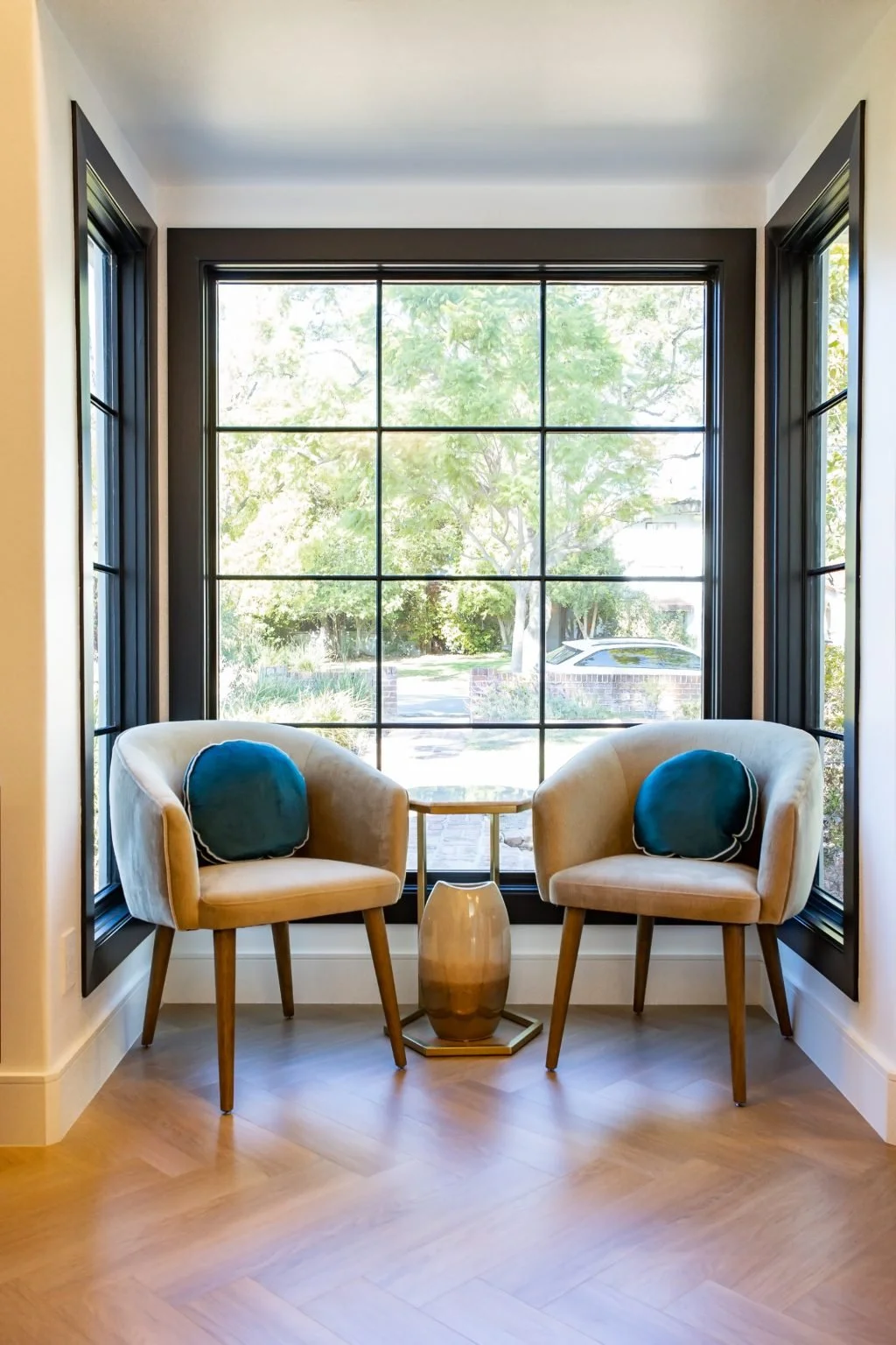 Two chairs in a black-framed bay window above herringbone wood floors