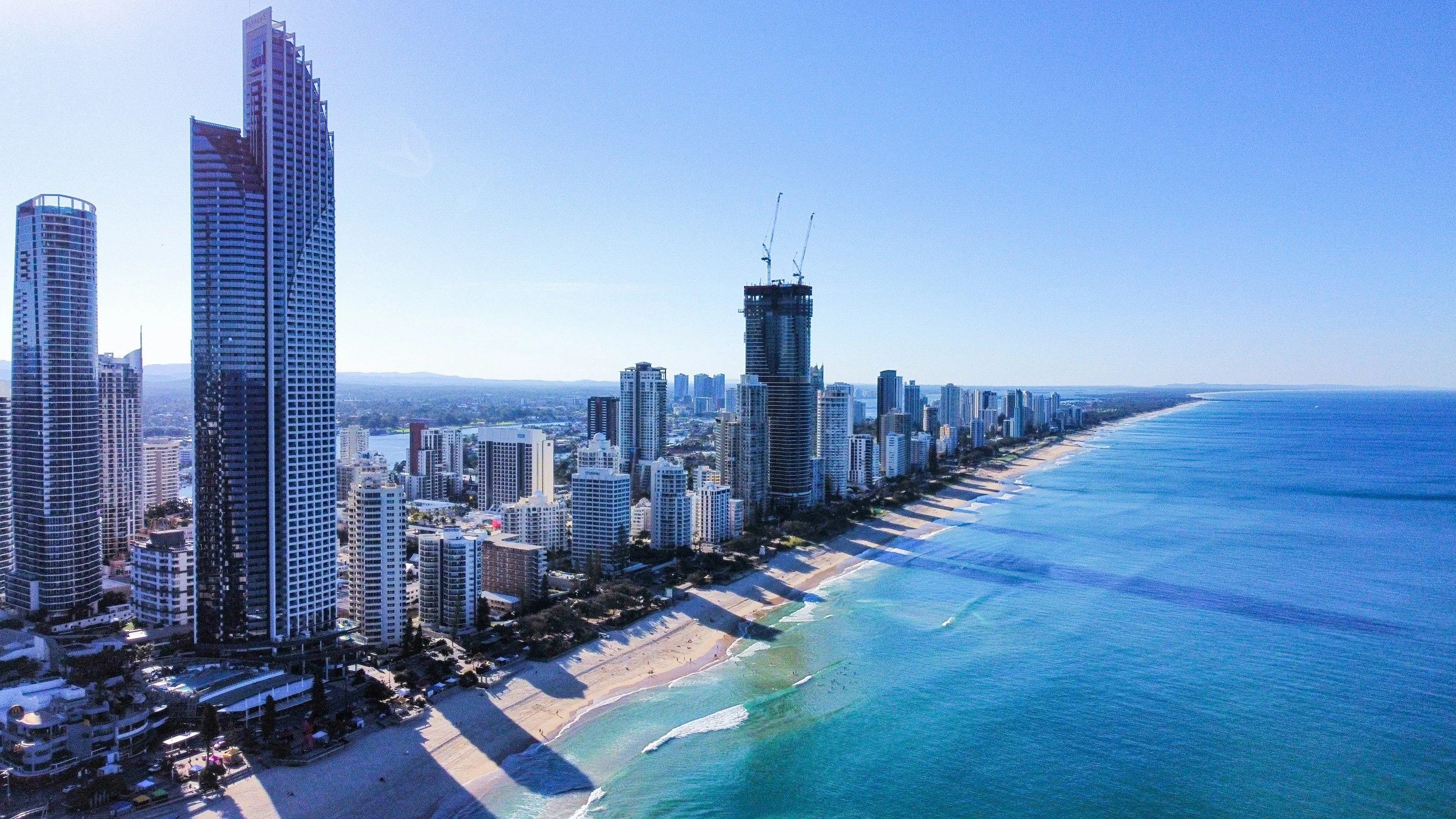 Aerial view of a city skyline with tall skyscrapers along a beach with blue water and white sandy shore.