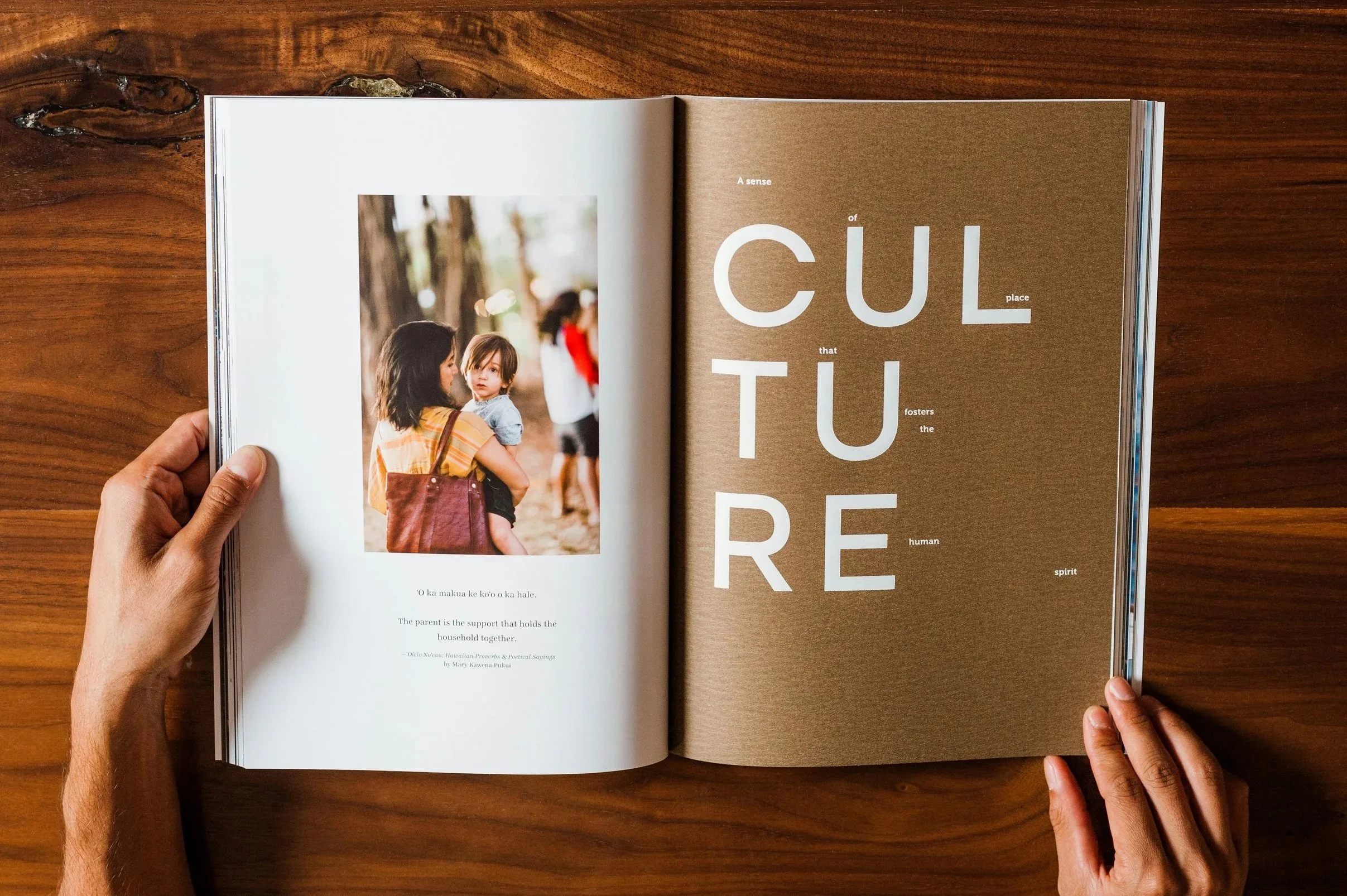 Open magazine on a wooden table, showing a photograph of a woman holding a child and large text on the opposite page.