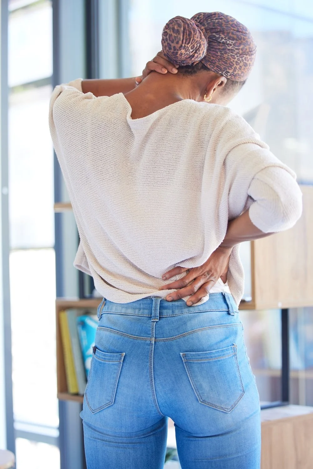 Woman holding her lower back, representing back discomfort and movement restriction during recovery.