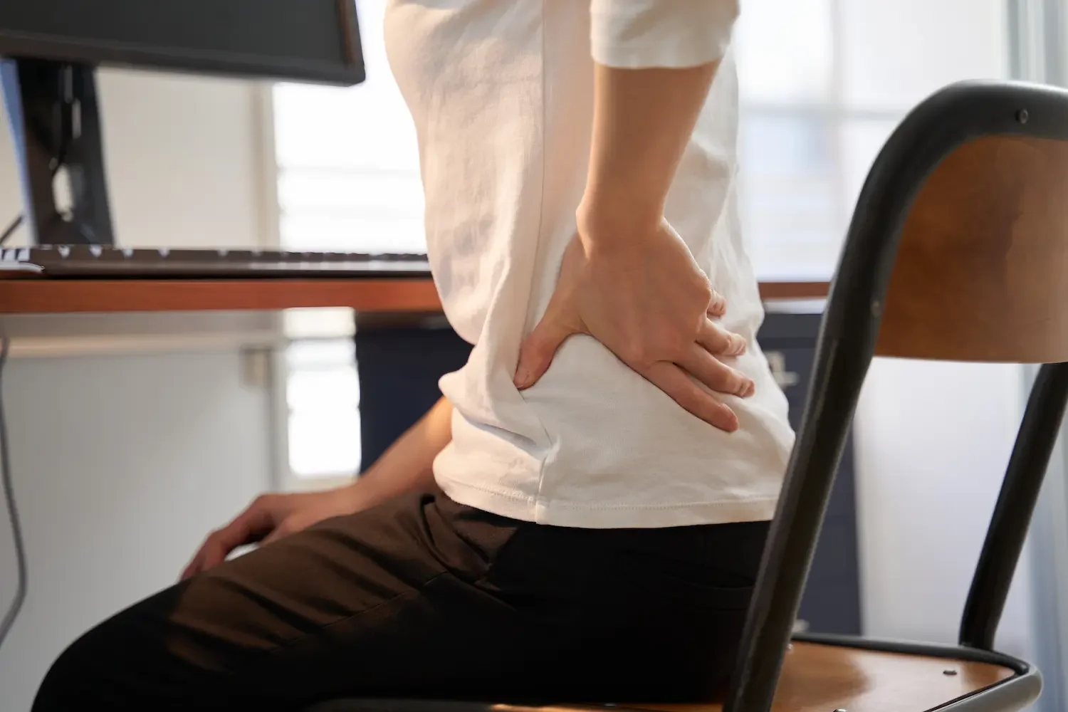 Person holding lower back with recurring back pain and stiffness