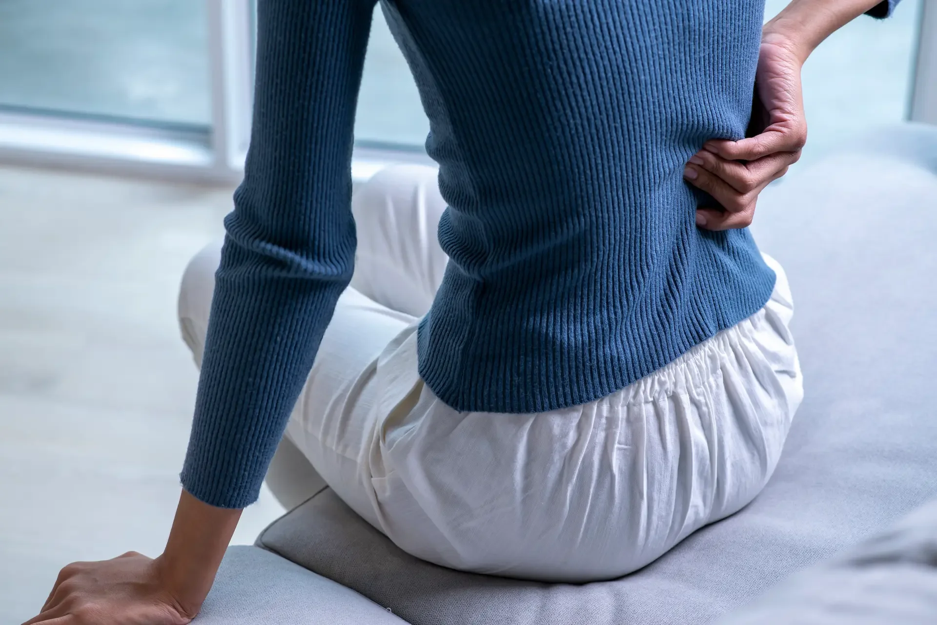 Person holding lower back with recurring back pain in Nelson