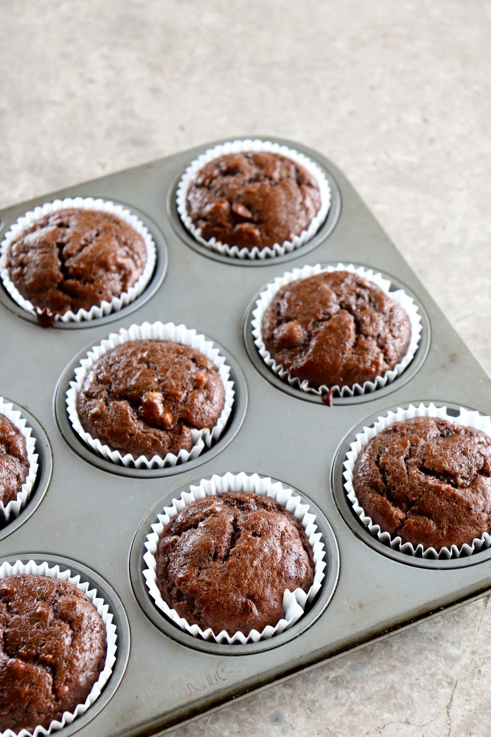 Chocolate muffins in a metal muffin tin on a marble countertop.