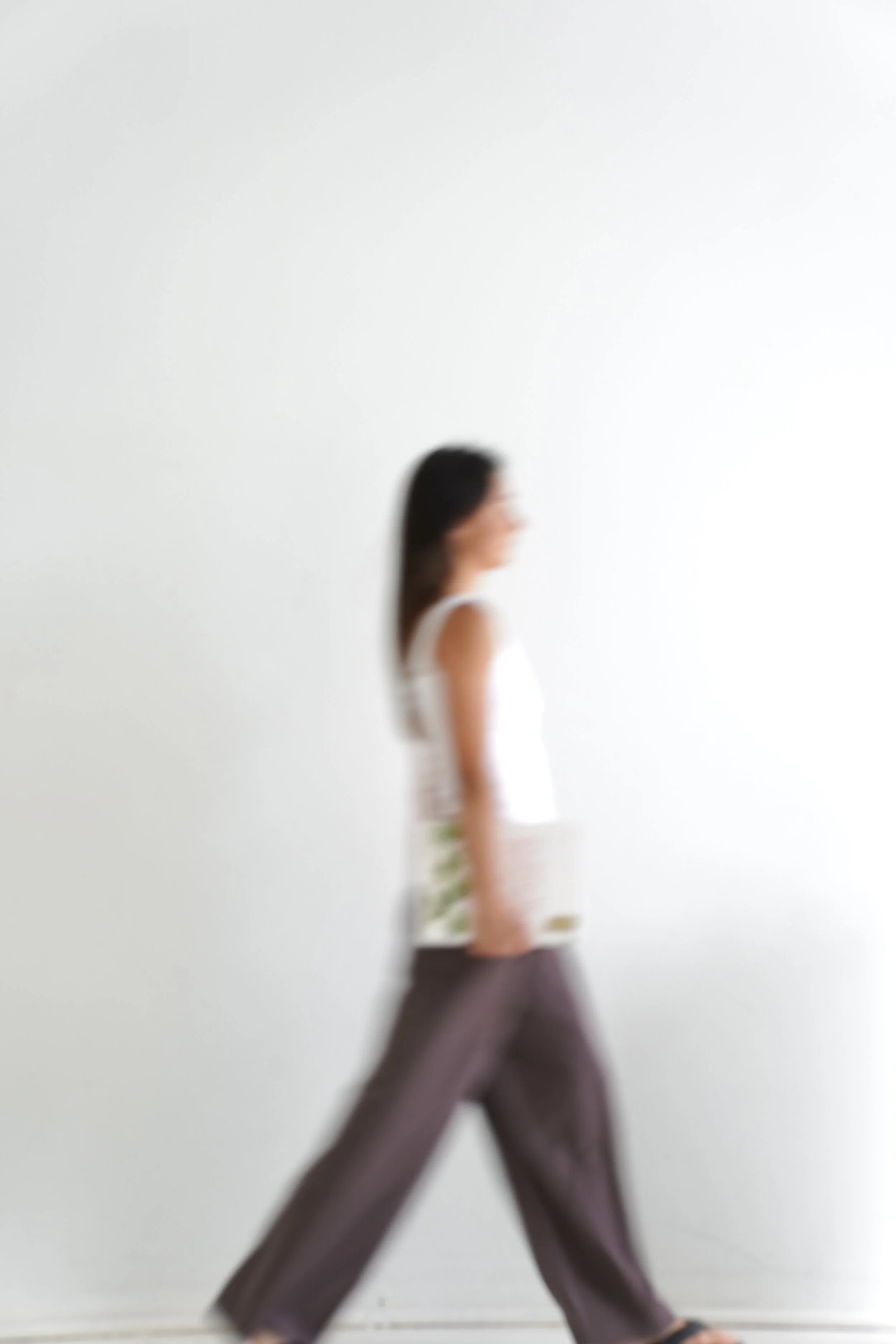 A woman walking past a plain white wall, seen in motion with blurred features.