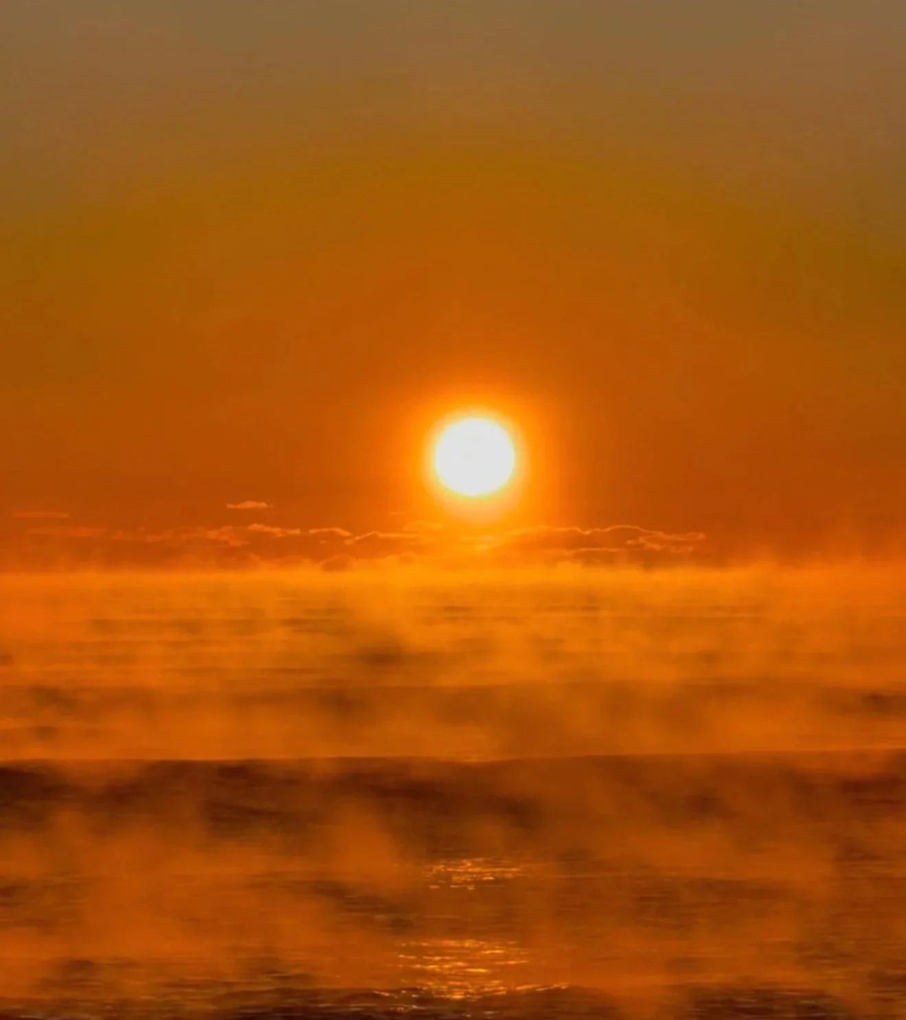 A sunset over the ocean with the sun near the horizon, casting a golden glow on the water and sky.