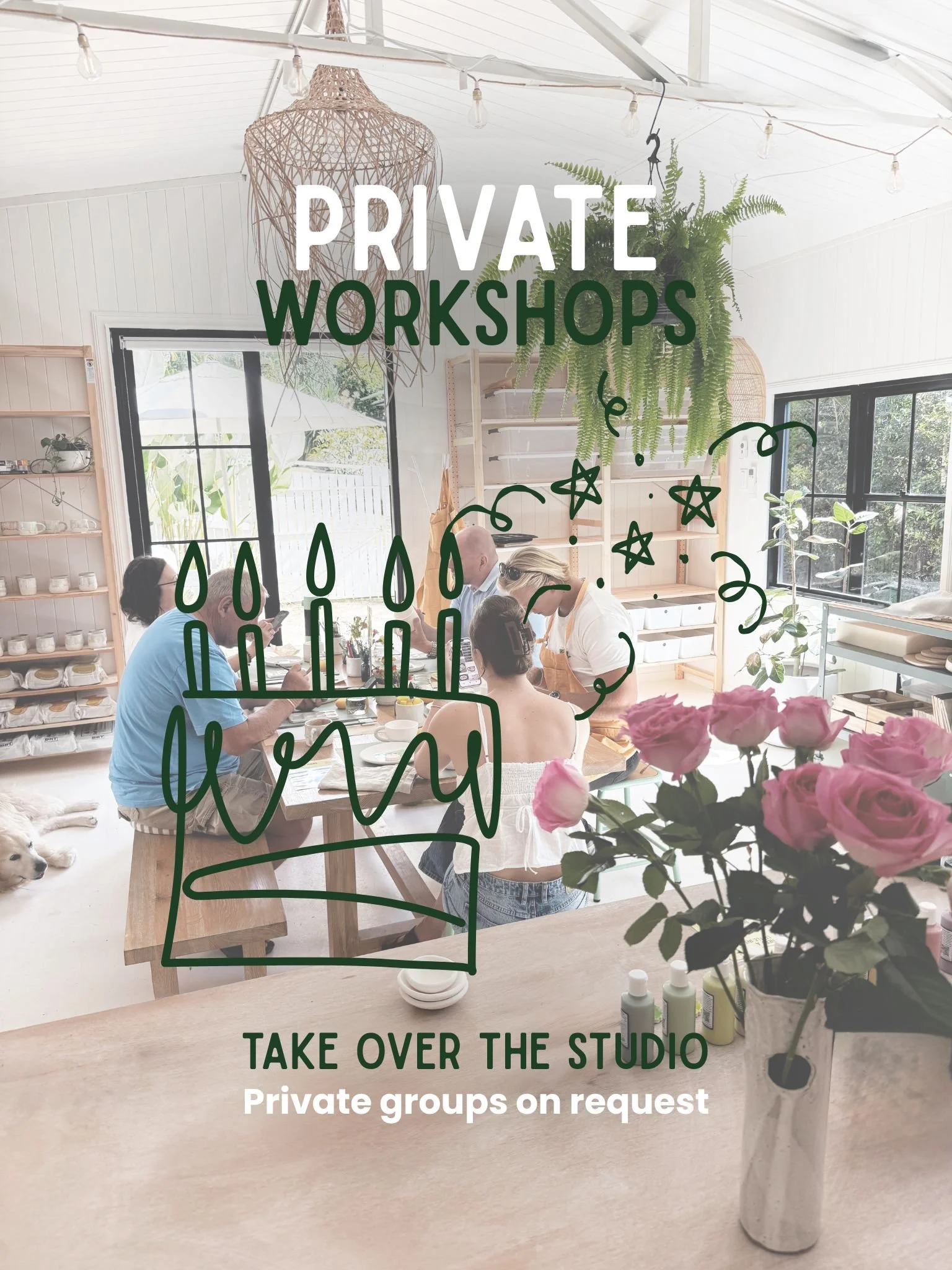 People sitting at a table in a bright, modern indoor space with large windows and green plants, engaged in a workshop or meeting, with a vase of pink roses in the foreground.