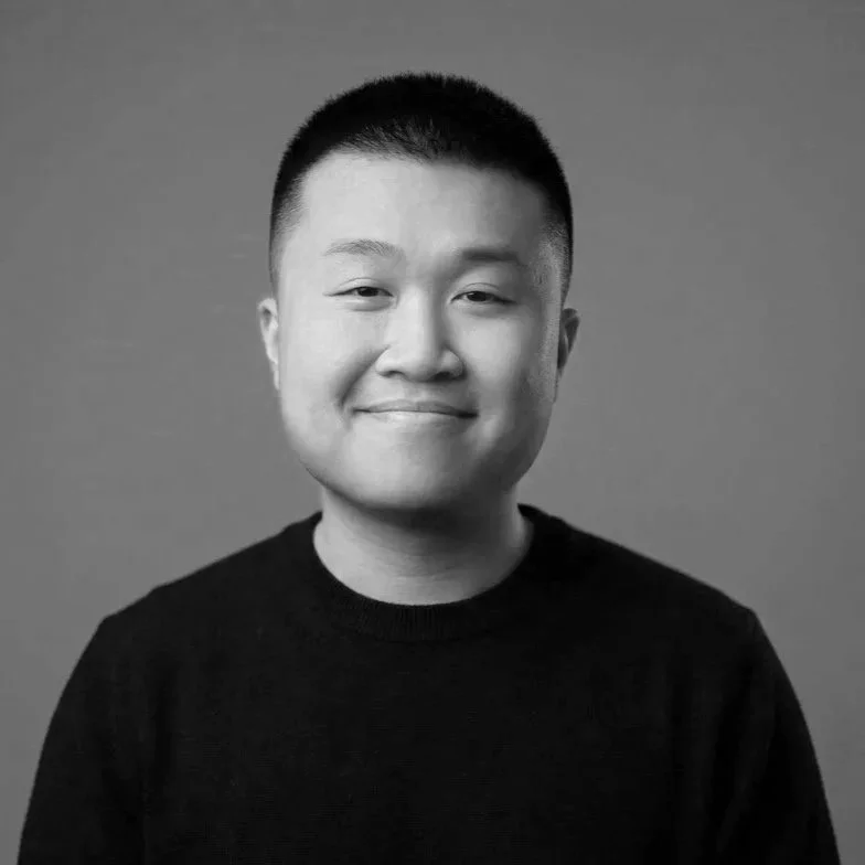 Young Asian man with short black hair, smiling, wearing a black shirt against a gray background.