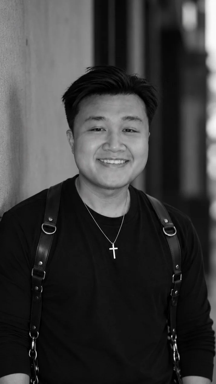 Young Asian man with short black hair, smiling, wearing a black shirt against a gray background.