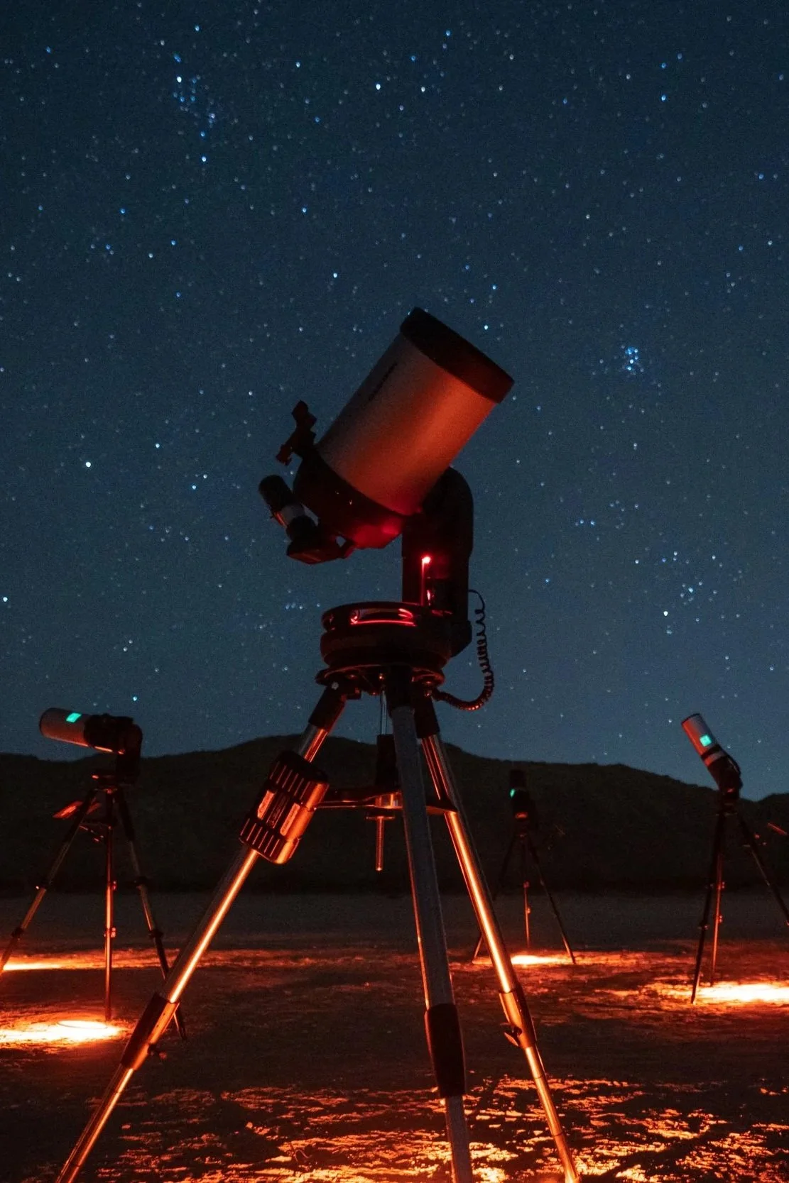 Stargazing Joshua Tree, Multiple telescopes set up outdoors at night beneath a starry sky, with distant mountains or hills in the background.
