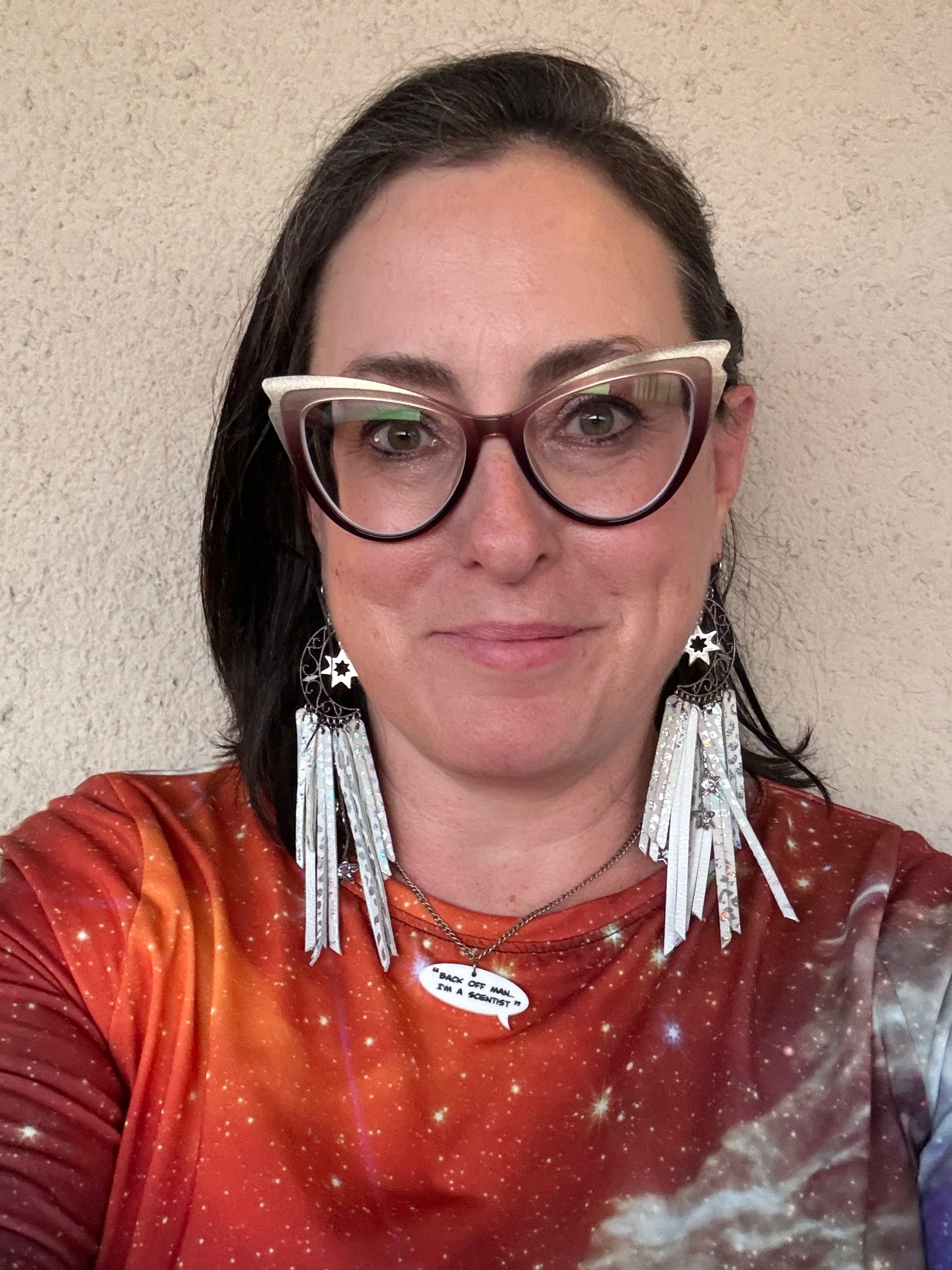 Summer Ash wearing large, colorful glasses, star-shaped earrings, and a red space-themed shirt. She has a sticker on her chest that reads "Back off man I’m a scientist."