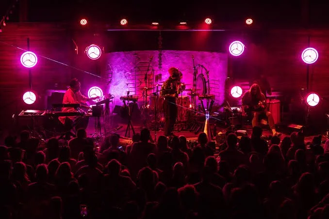 Band performing live on stage with colorful lighting, audience watching in front.
