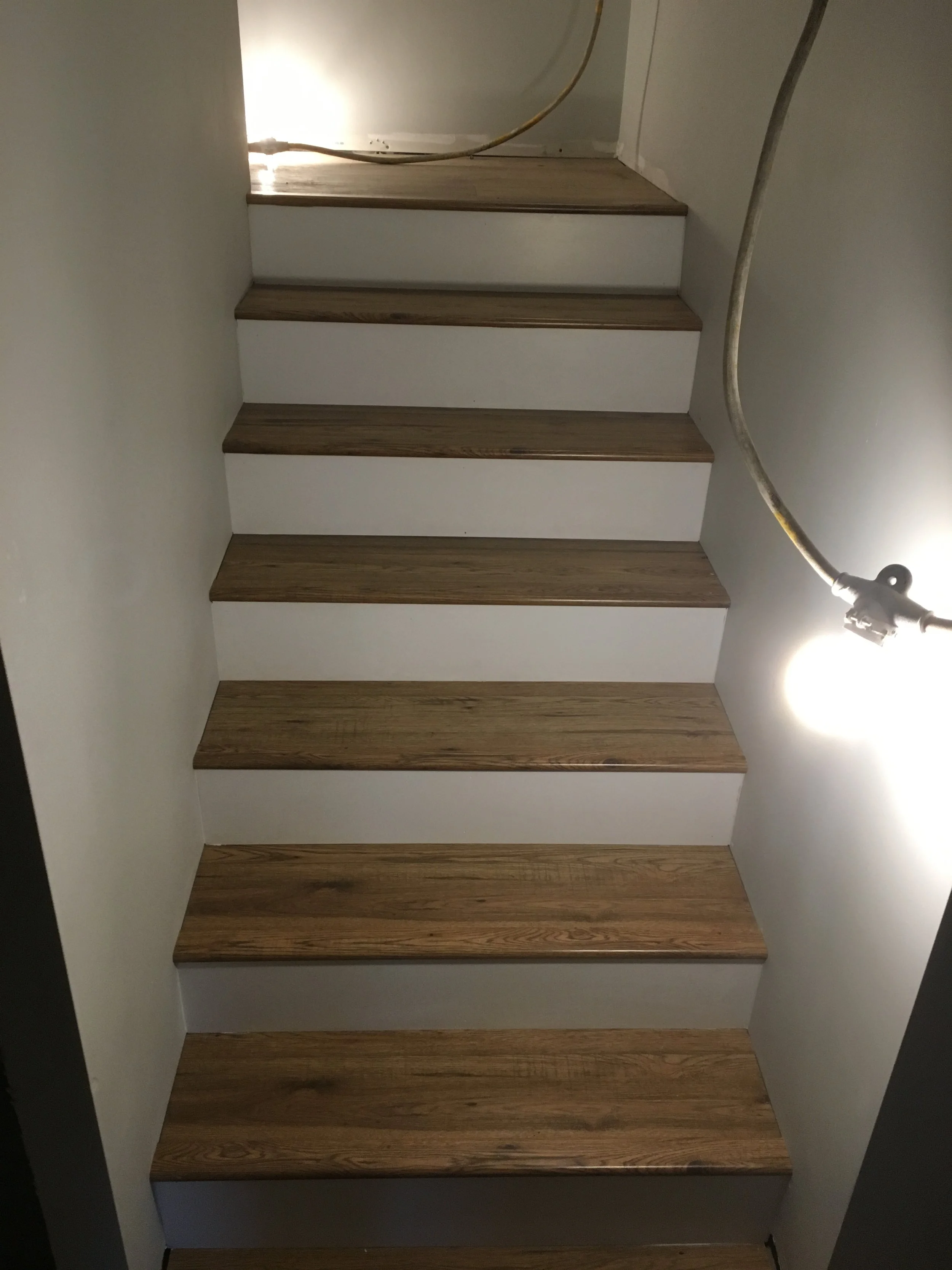 Wooden stairs with a white stair riser and a ceiling light shining down.