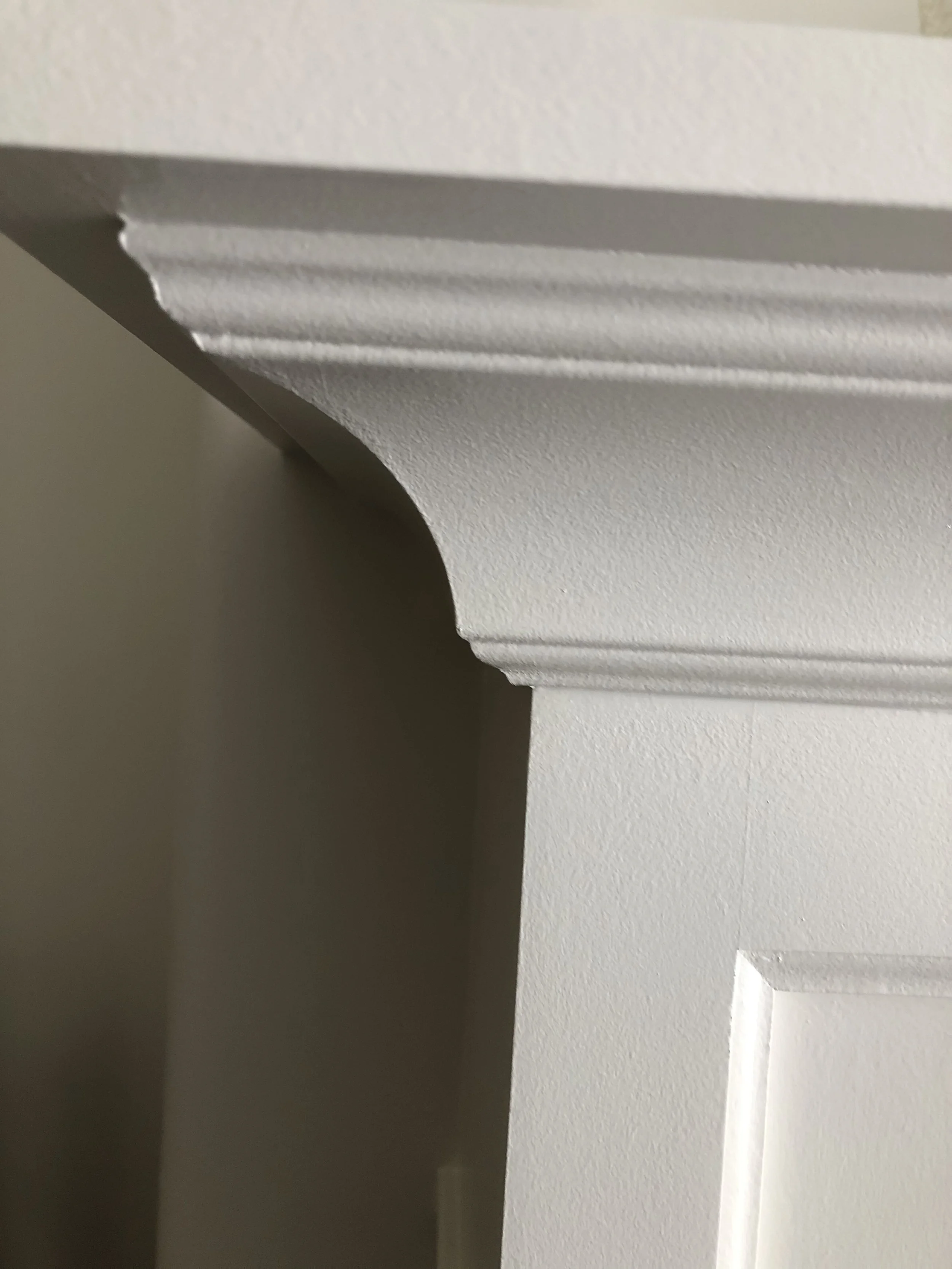 Close-up of a white crown molding or decorative trim at the ceiling corner, showing detailed edges and shadow effects.