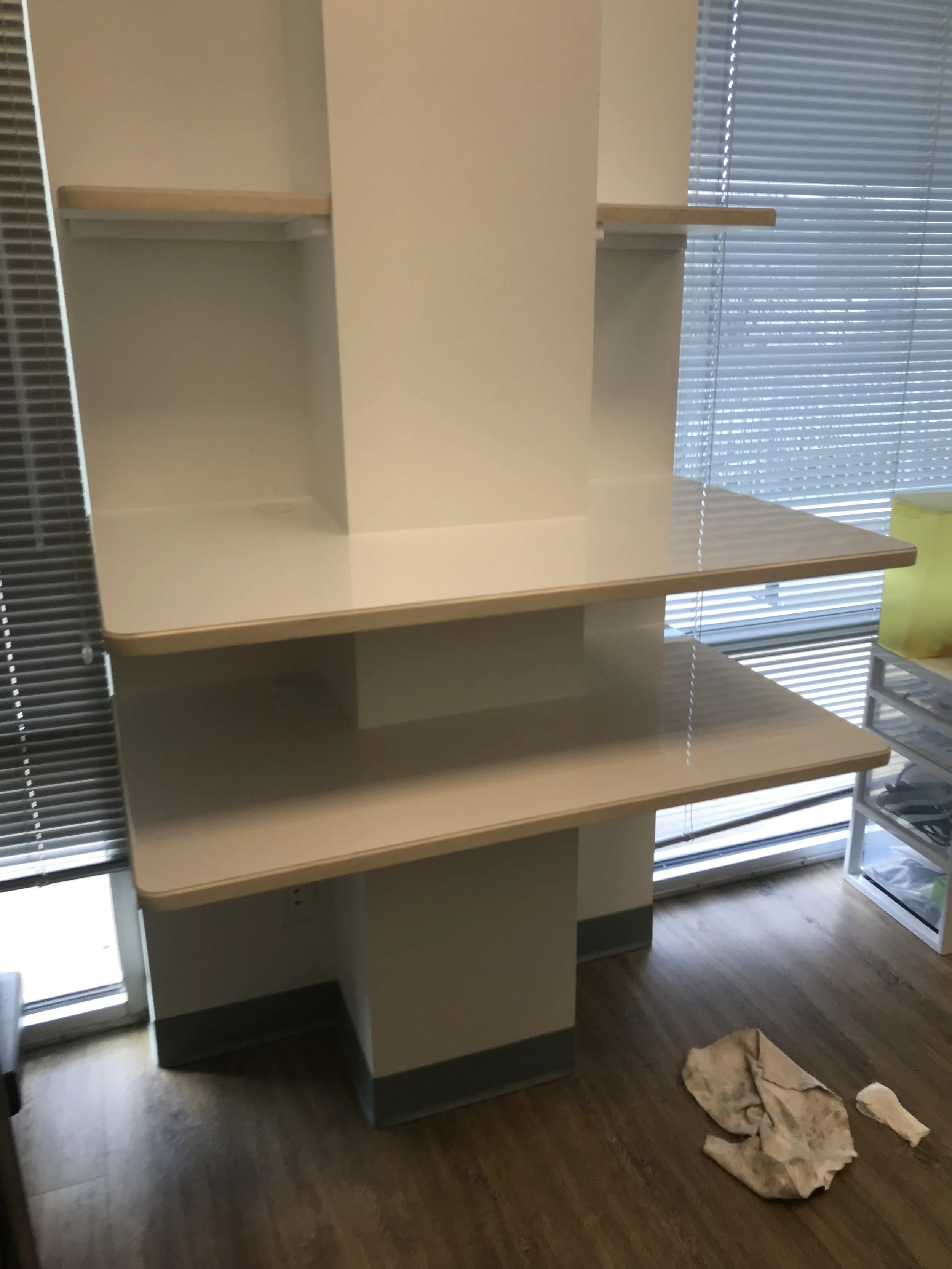 Empty office or classroom space with beige shelving units, window blinds, and scattered cloths on the floor.