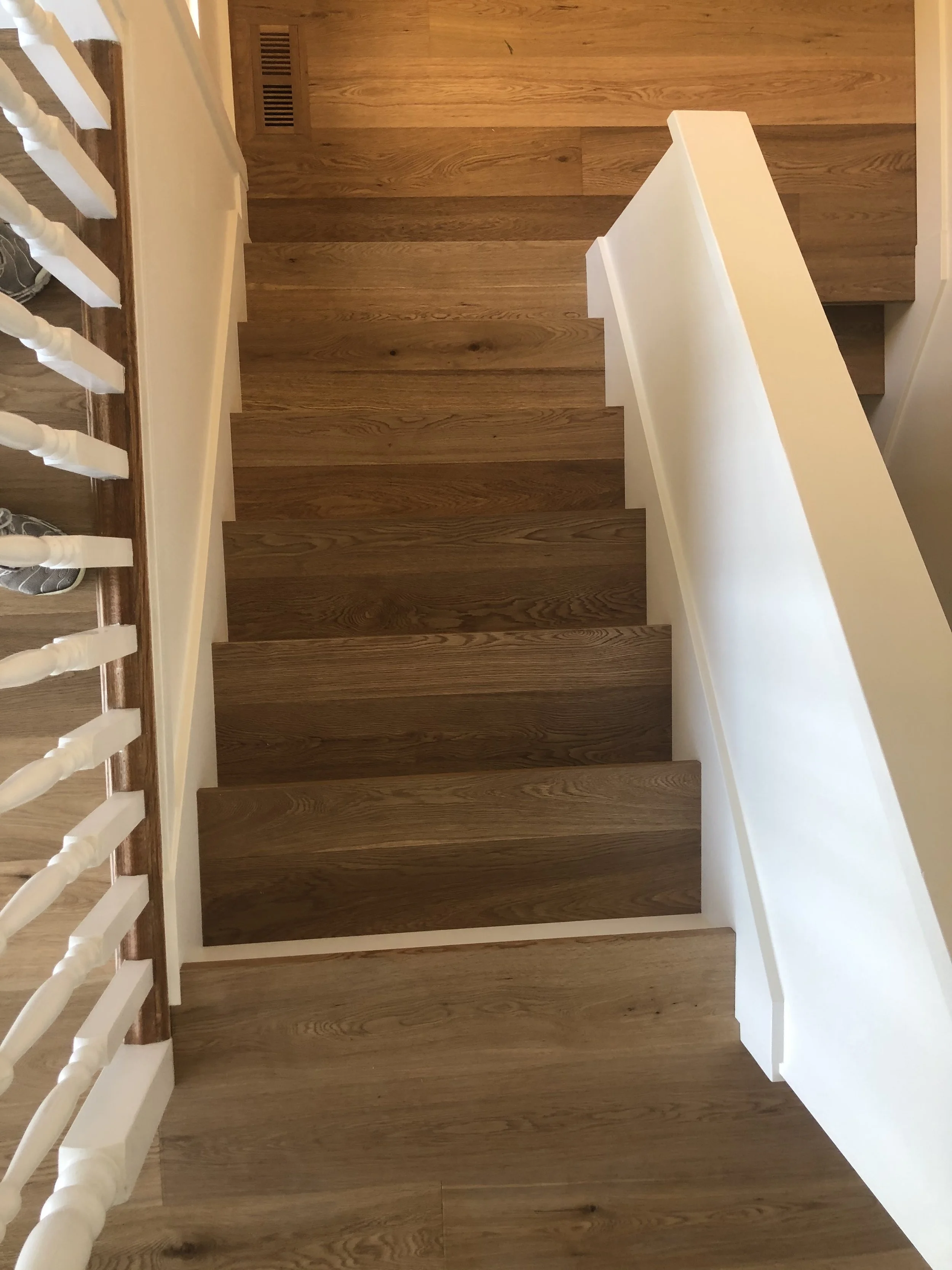 Top-down view of a wooden staircase with white railings and a beige wall on the left side.