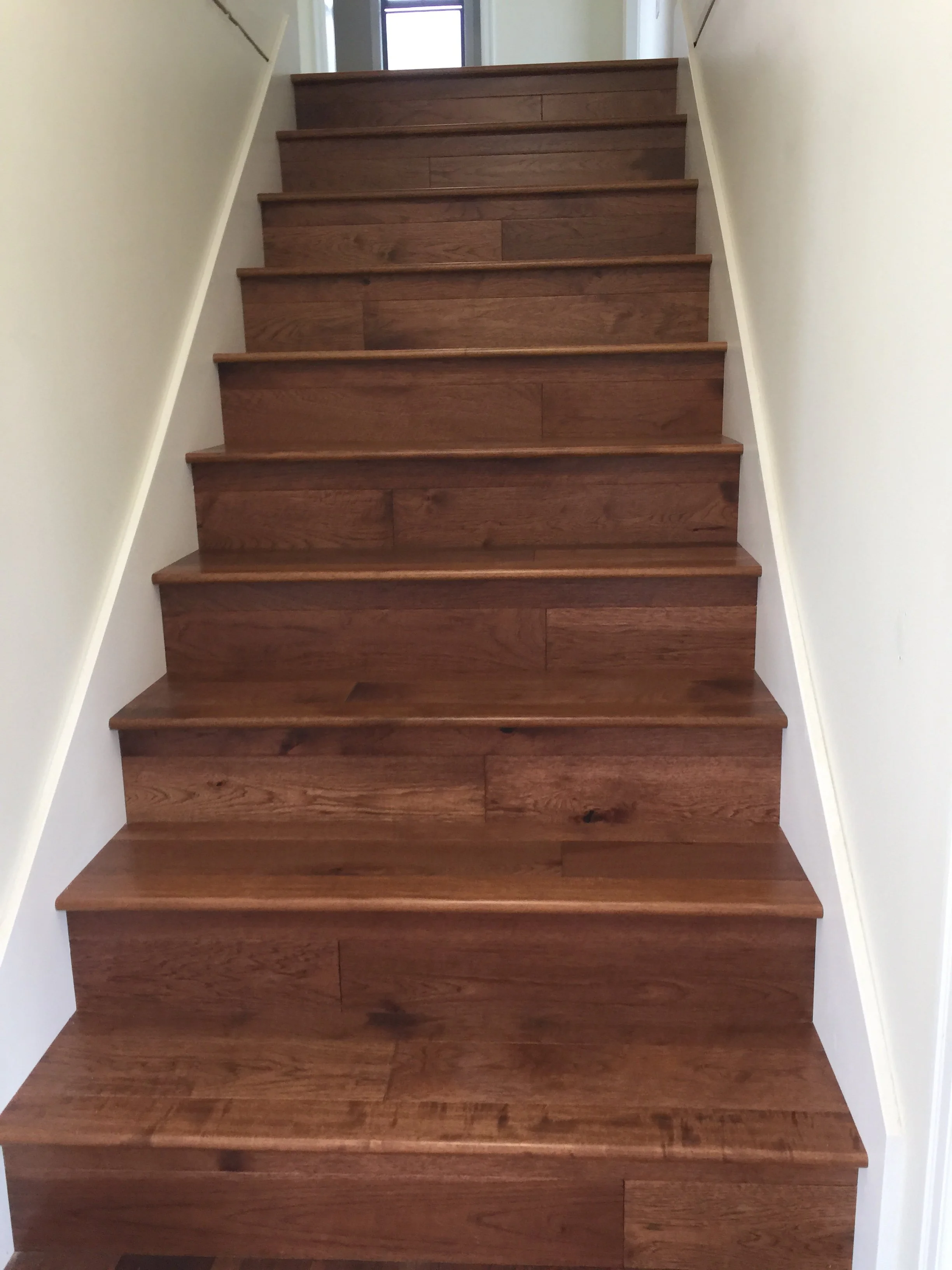 A staircase with wooden steps and white walls on either side, leading up to a door with a window at the top.