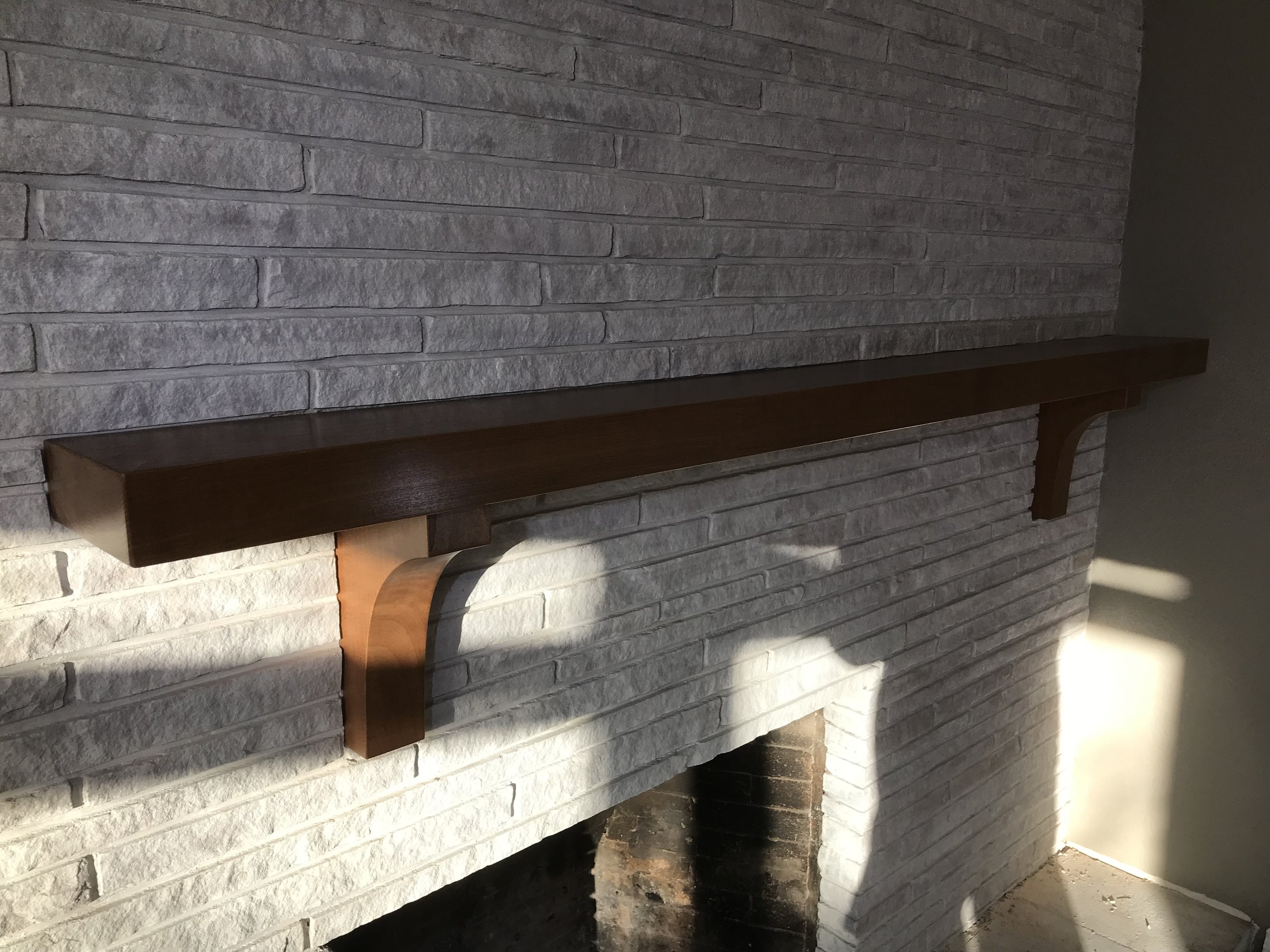 Interior view of a fireplace with a white brick surround and a wooden mantel, with a small fire burning inside.