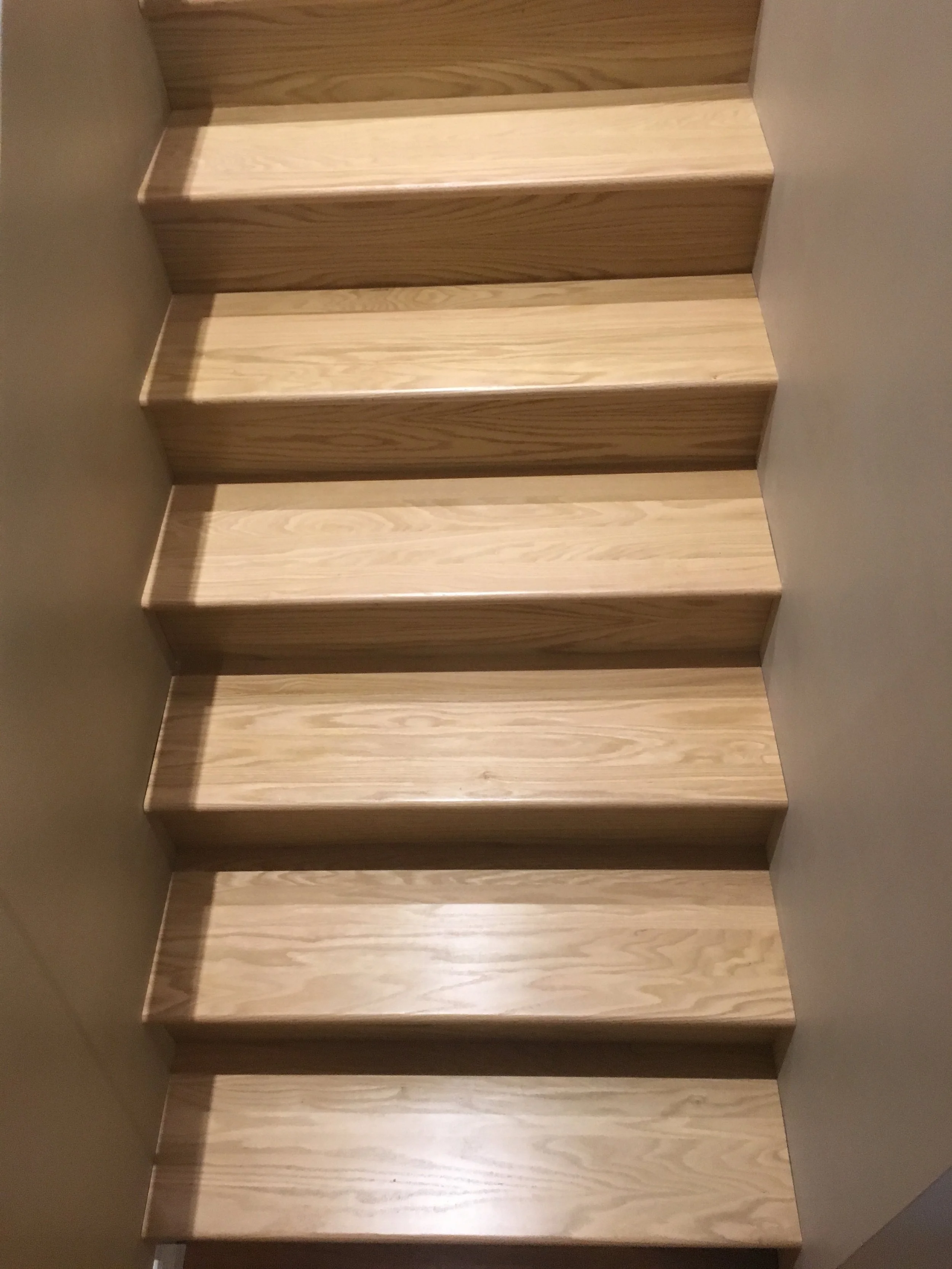 Wooden staircase with five steps, viewed from below, ascending from bottom to top.