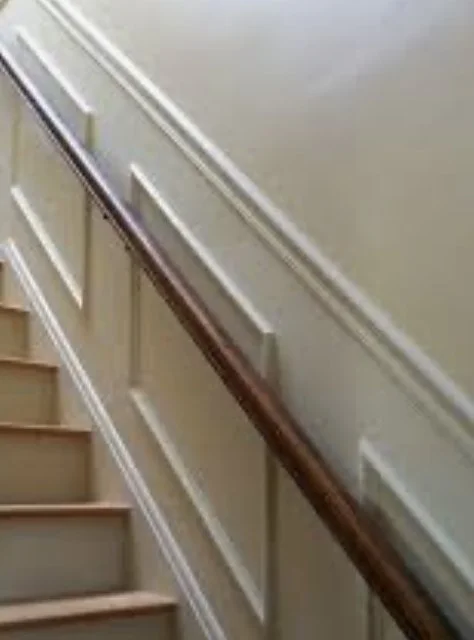 A staircase with wooden handrail and beige wainscoting, viewed from the bottom looking upward.