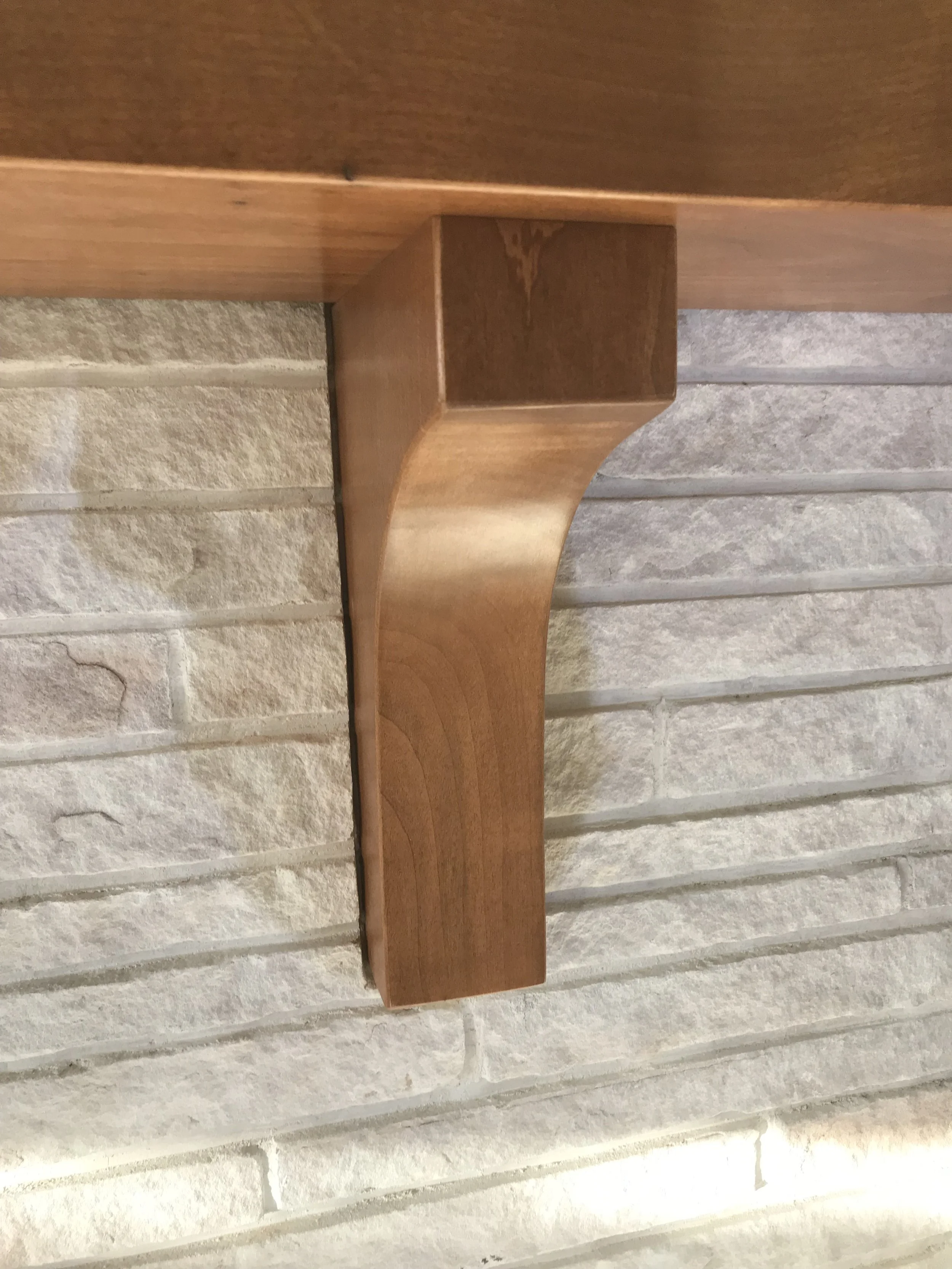 Close-up of a wooden shelf bracket attached to a white brick wall.