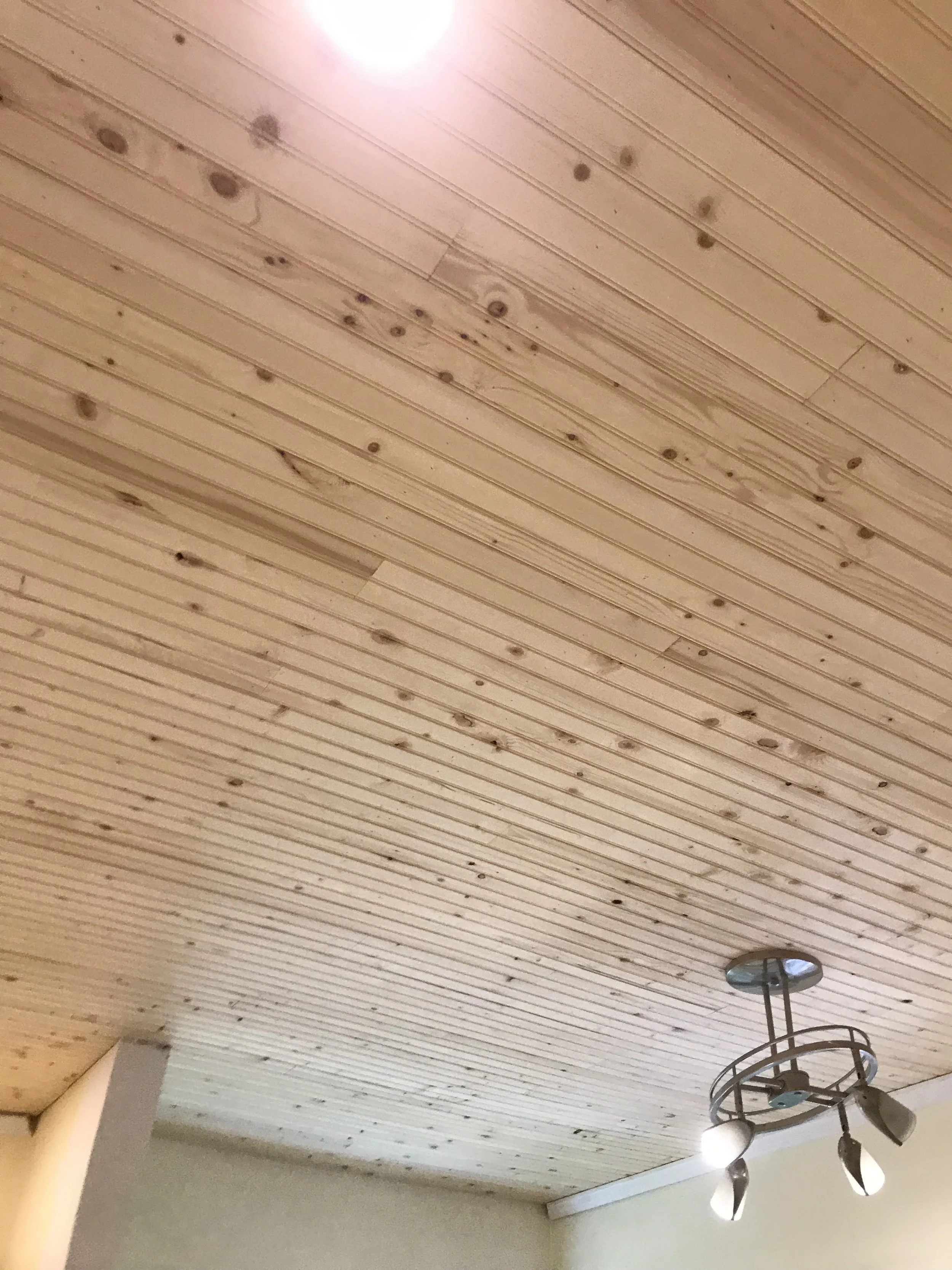 Wooden ceiling with a light fixture and a ceiling fan in a room.