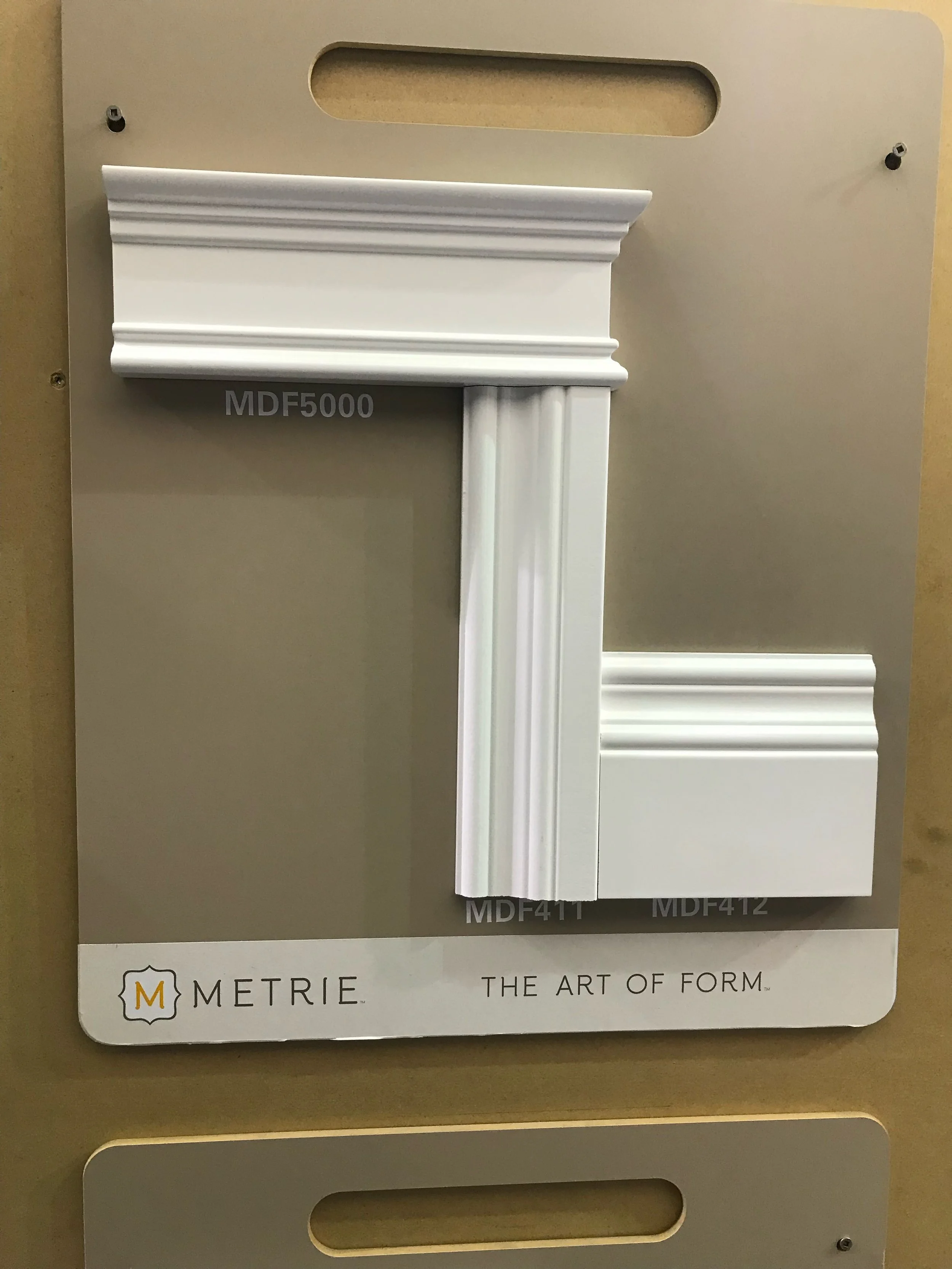 Sample display of architectural moldings with various styles and finishes on a board labeled "METRIE: The Art of Form".
