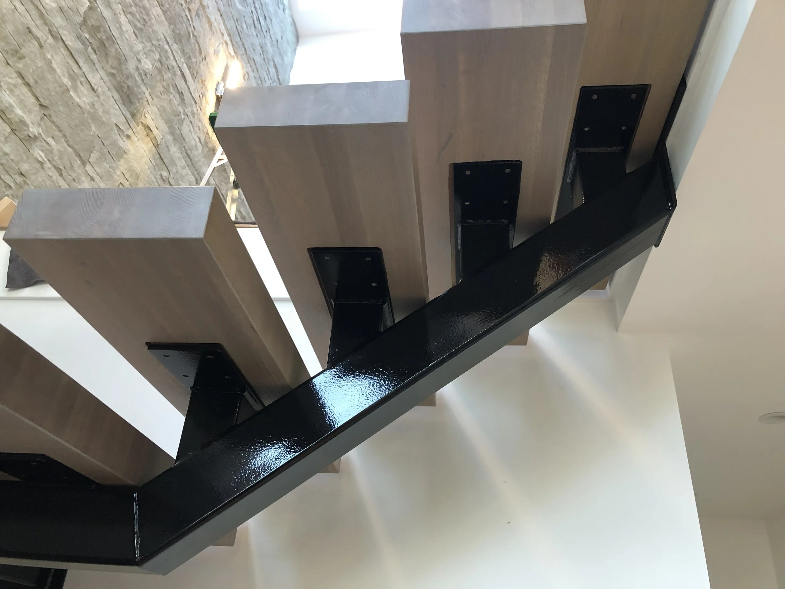 Close-up of a modern, minimalist wooden and metal staircase with black rails and a brick wall in the background.