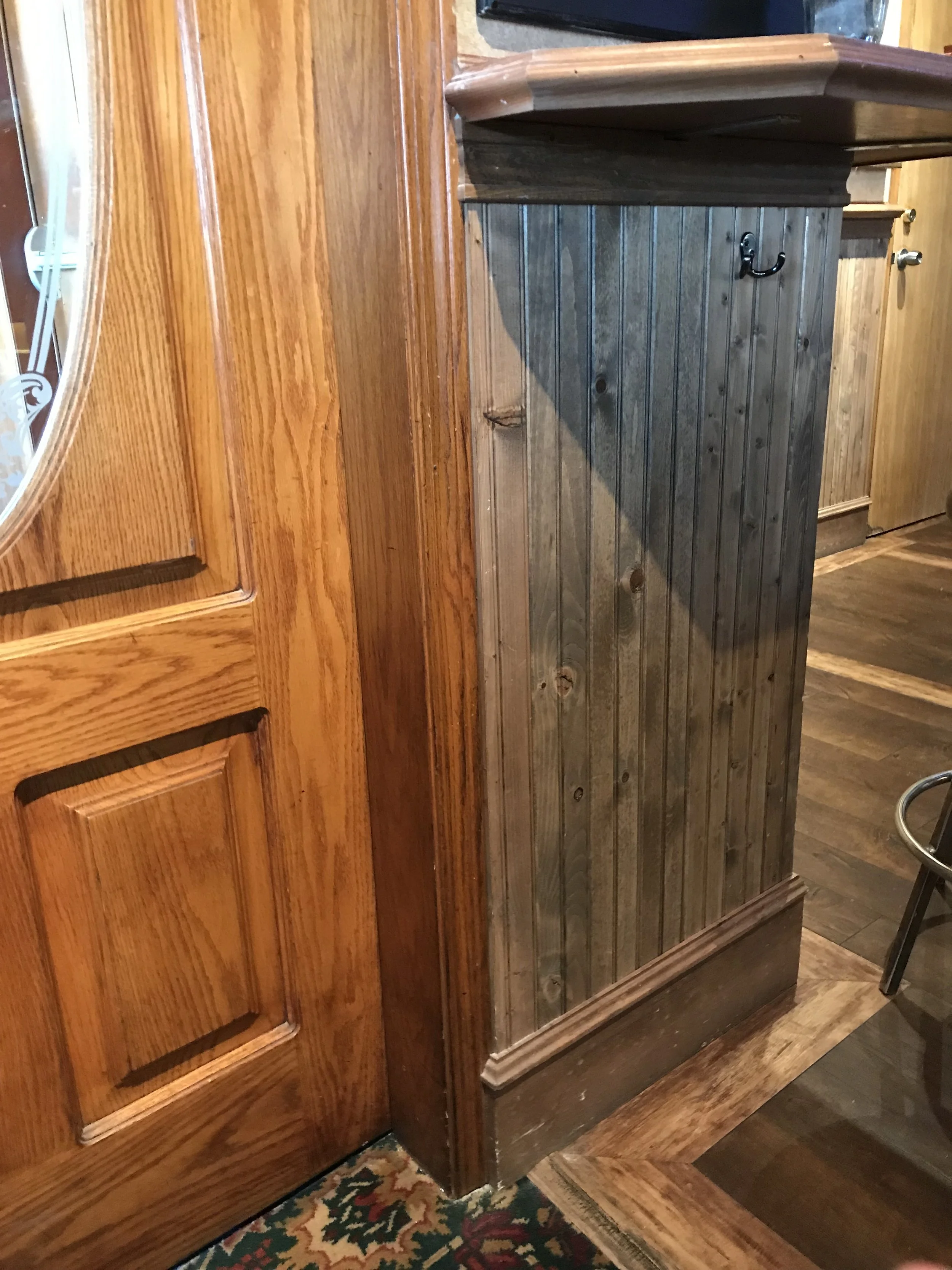 A wooden cabinet and a wooden bar at a restaurant or bar, with a carpeted floor and hardwood floors.