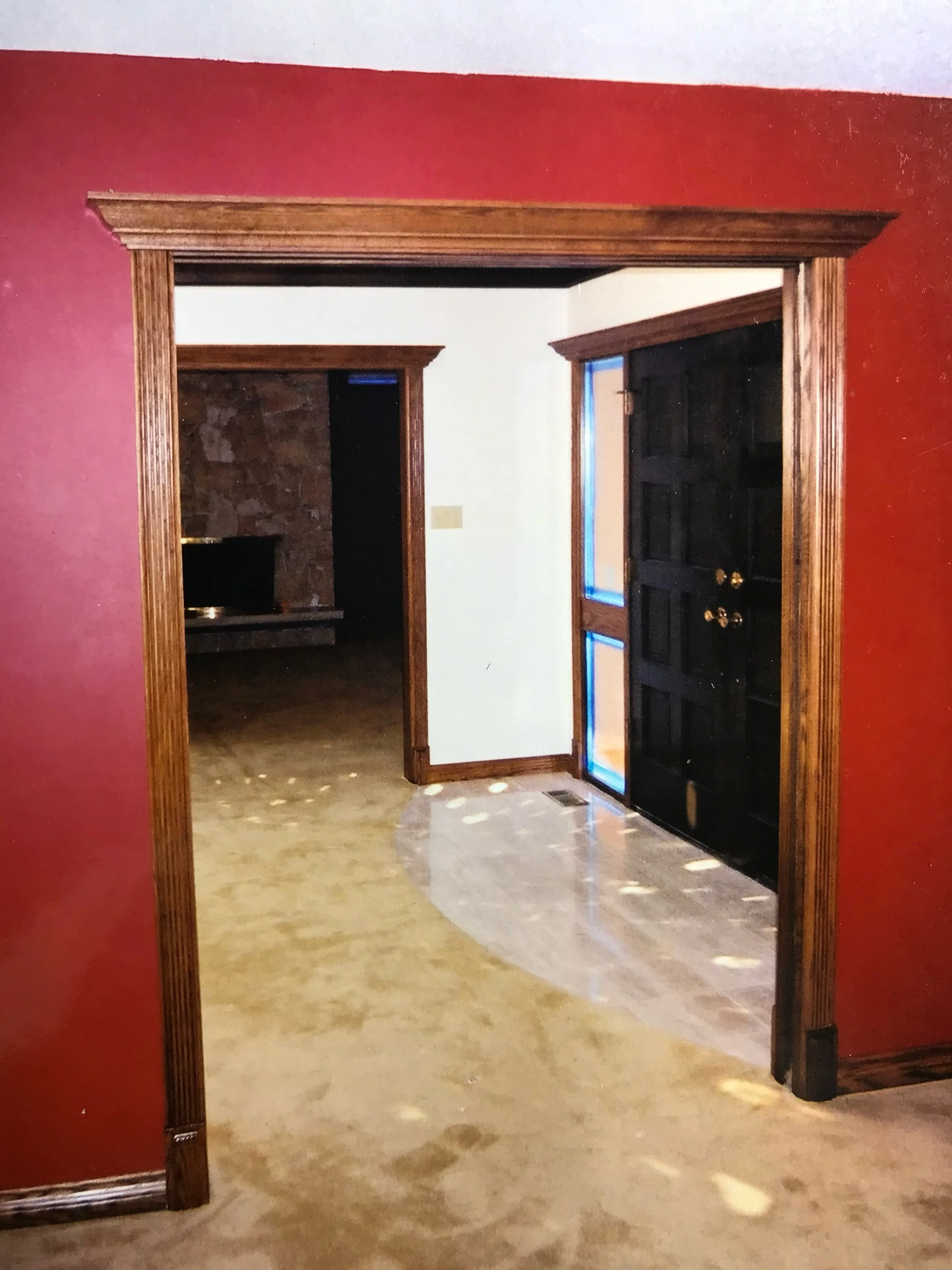 View through a doorway into a room with a black door and stone fireplace. The room has white walls and wooden trim.