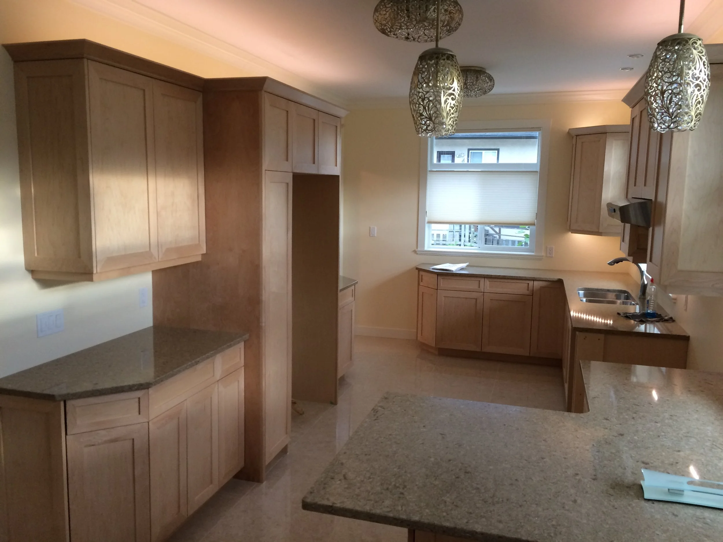 Kitchen with wooden cabinets, granite countertops, and pendant lights hanging from the ceiling. There is a window with blinds above the sink area.