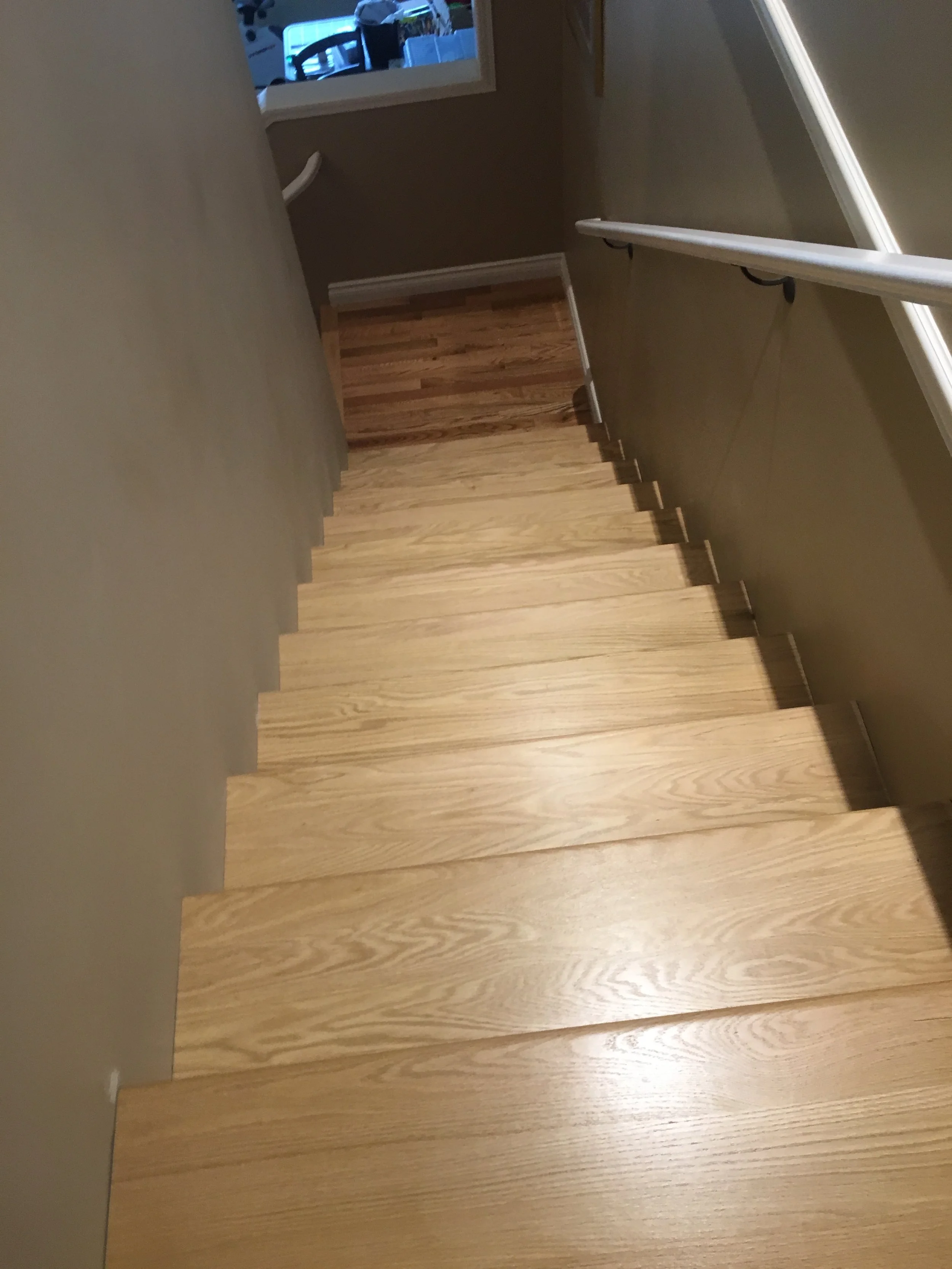 A staircase with wooden steps, a handrail on the right side, and a partially visible top landing with a window showing another room with furniture.