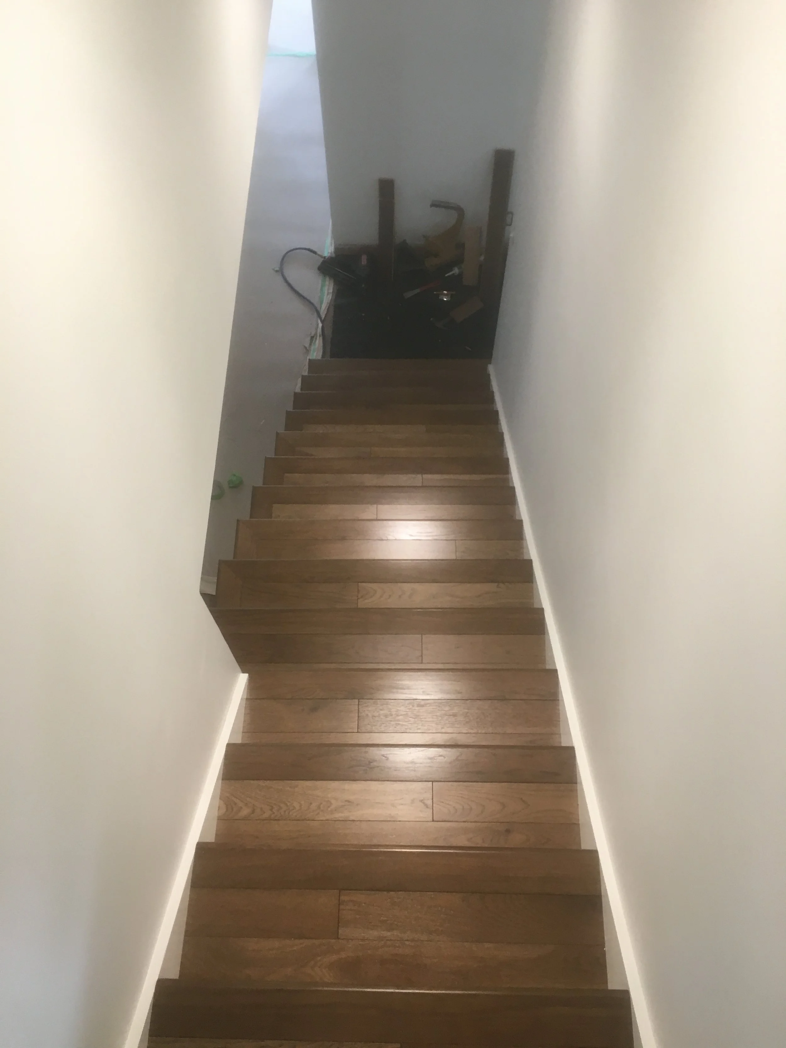 Indoor staircase with wooden steps, white walls on either side, leading to a landing with construction tools and supplies.