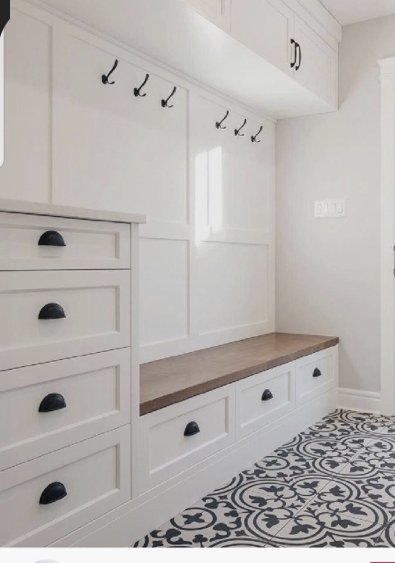 Entryway with white built-in cabinets, a wooden bench with drawers, black hooks on the wall, and patterned black and white tile flooring.