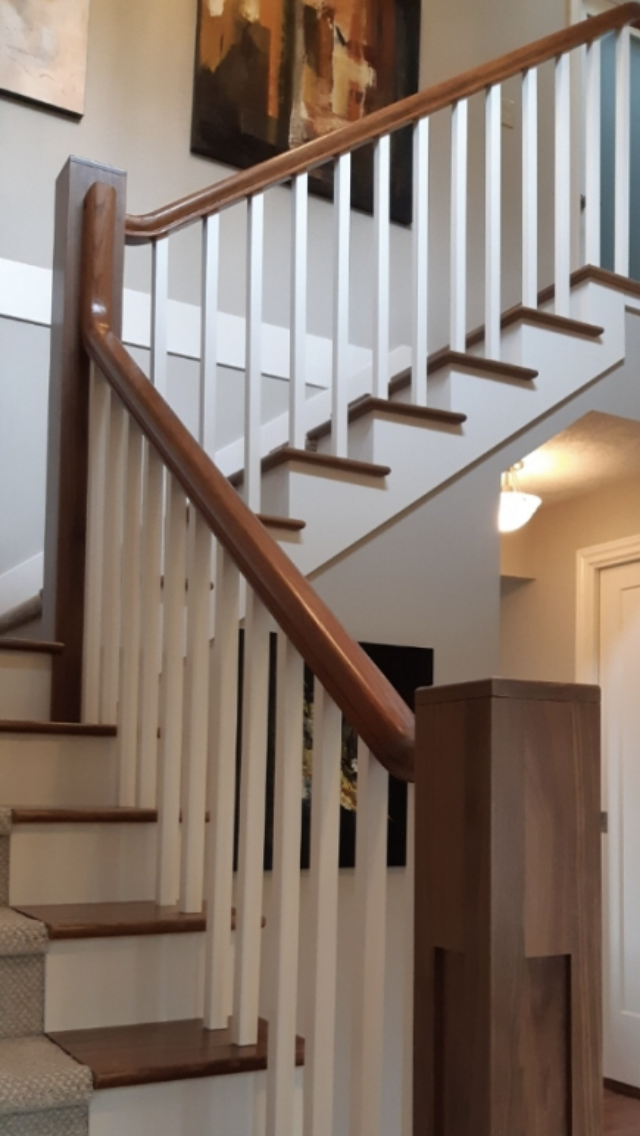 A staircase with a wooden handrail, white spindles, and brown steps leading to an upper floor, with artwork hanging on the wall in the background.